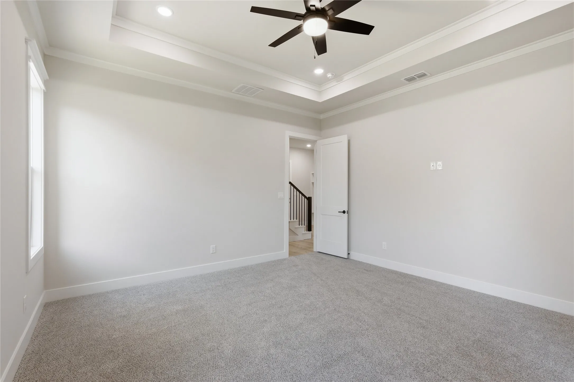 Carpeted room featuring a tray ceiling with recessed lighting and a ceiling fan, white baseboards, and a window for natural light