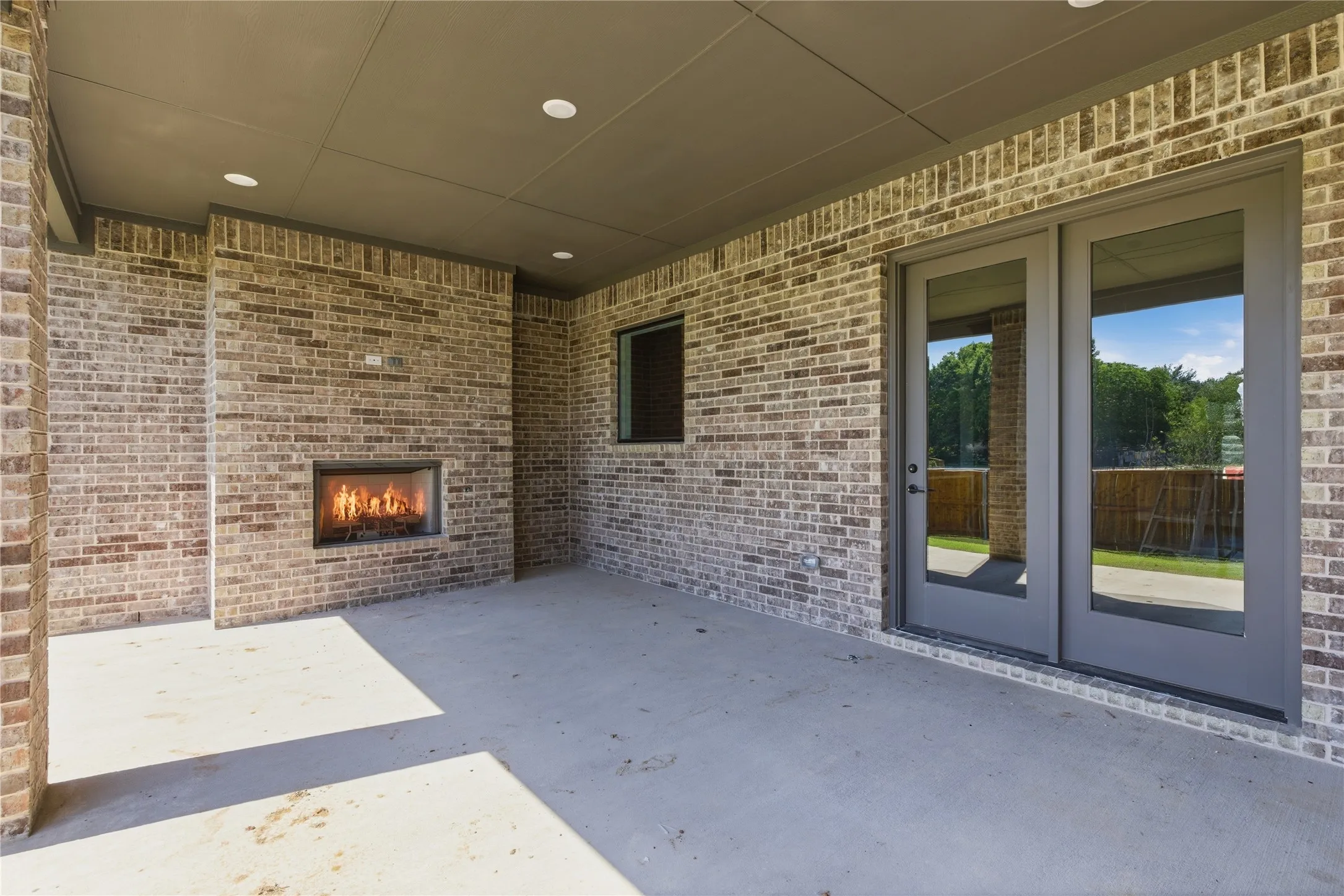 Covered outdoor patio featuring a built-in fireplace, brick construction, recessed lighting, and double glass doors