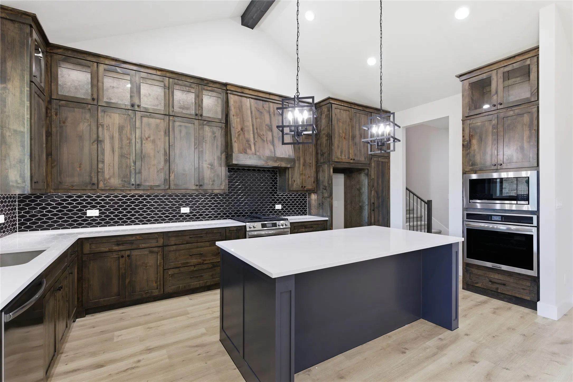 Kitchen featuring a central island, dark wood-finish cabinetry, light wood-finish flooring, a herringbone mosaic tile backsplash, and stainless steel appliances