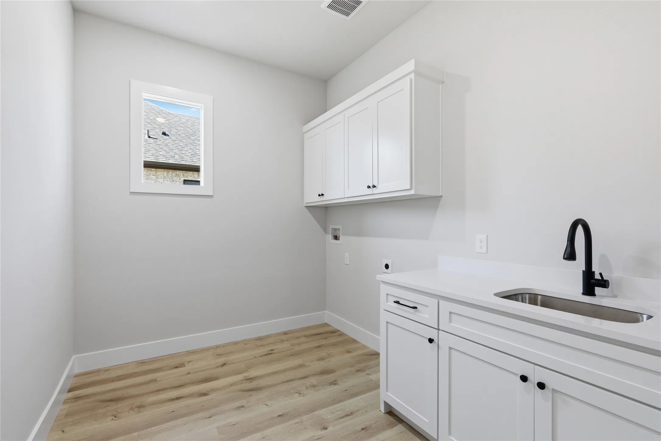 Utility space featuring white cabinetry, a single basin sink with a black gooseneck faucet, light wood-finish flooring, and a window