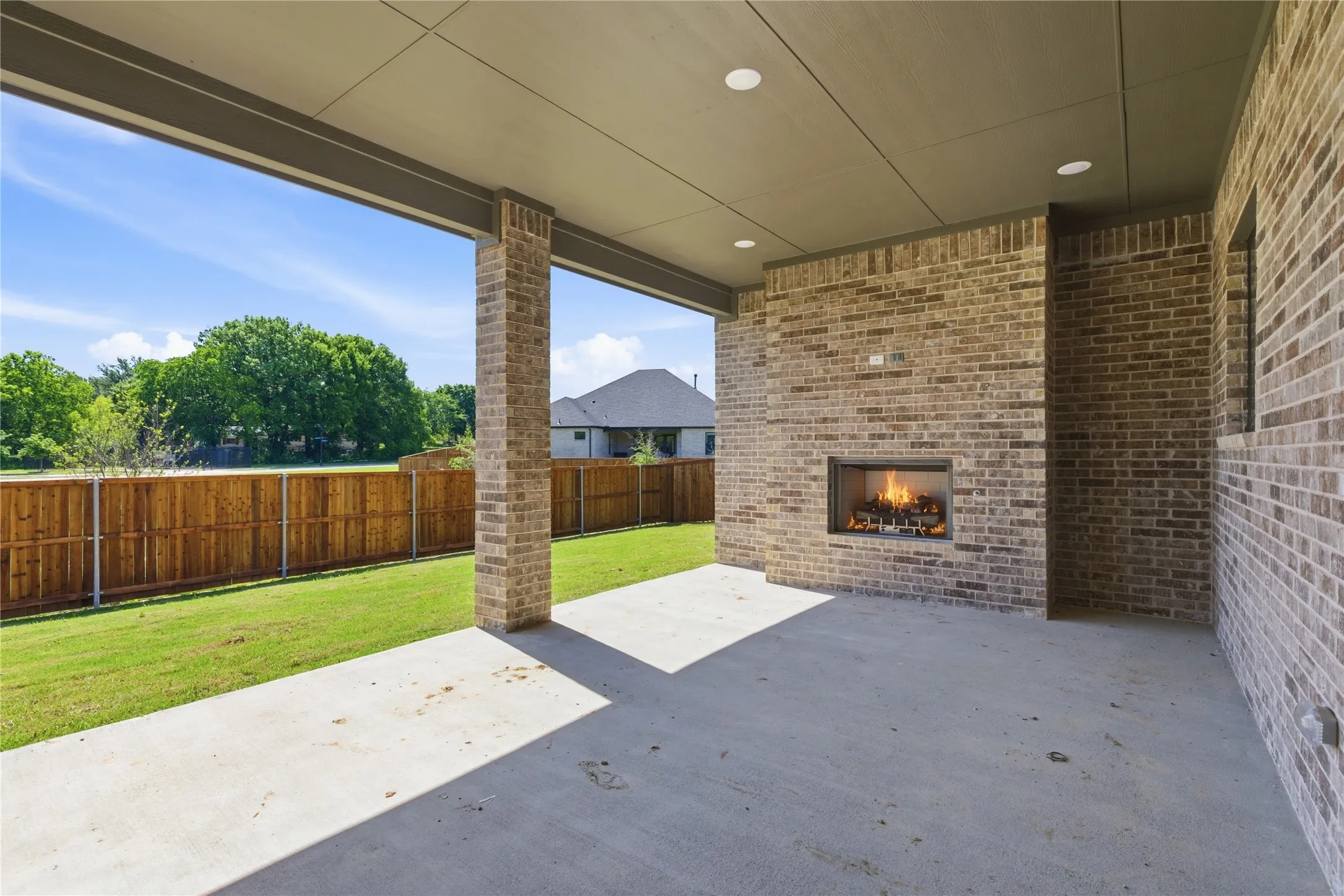 Covered patio featuring an outdoor fireplace with a recessed firebox, brick exterior, concrete flooring, and recessed lighting