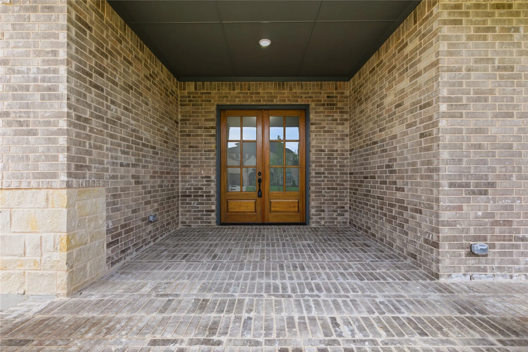 Covered entryway featuring a double wood-paneled door with glass inserts, brick-patterned flooring, and a recessed ceiling light fixture