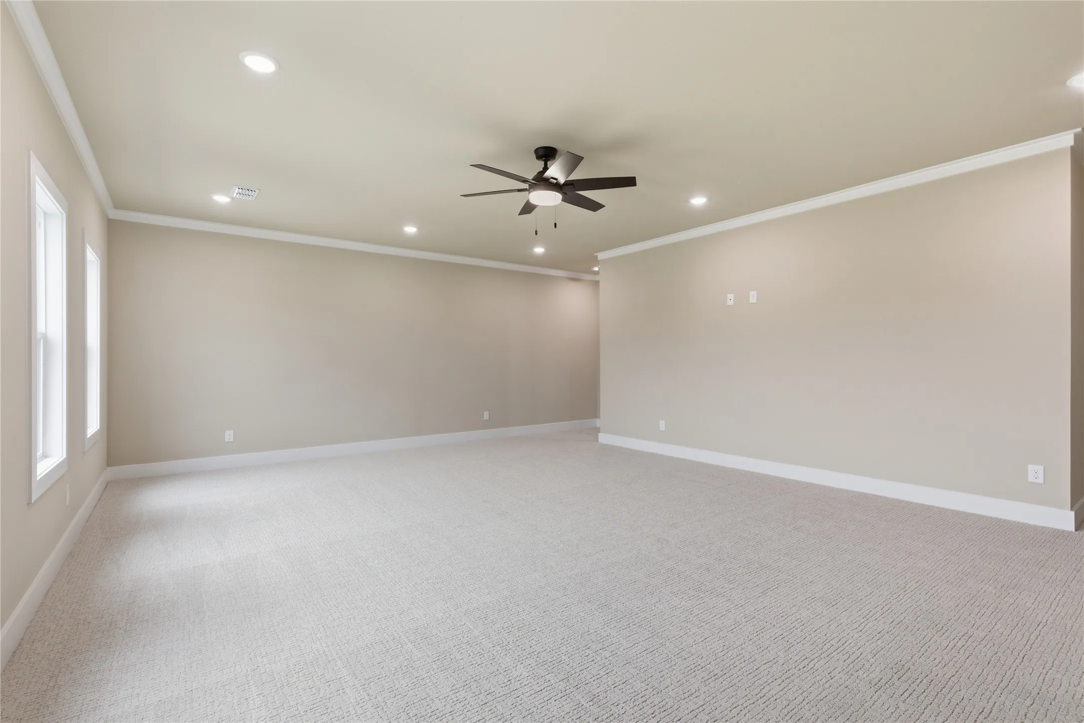 Expansive room featuring light-toned carpeting, ample recessed lighting, a ceiling fan, and multiple windows