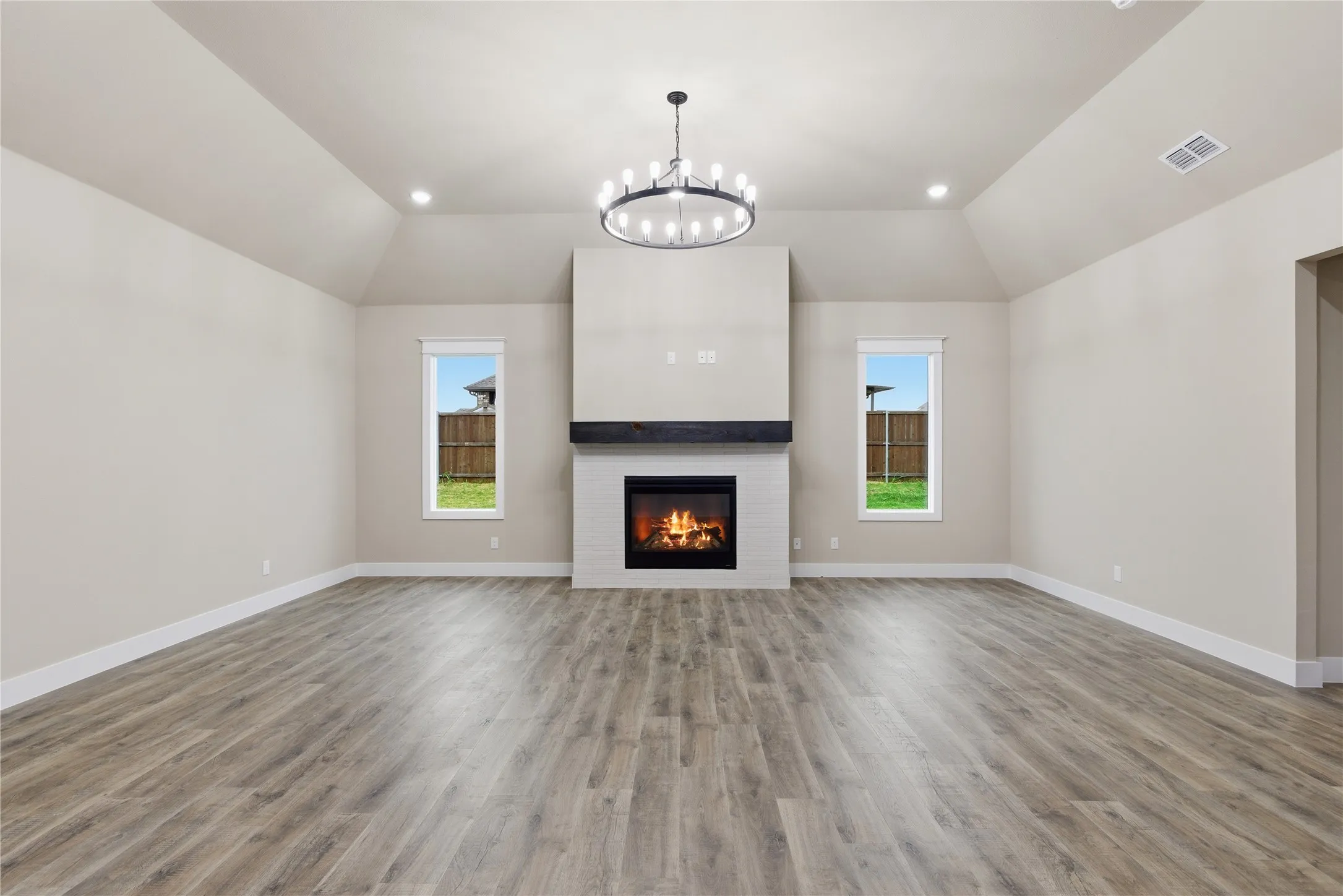 Spacious room featuring vaulted ceilings, a central fireplace with a white tile surround and dark wood mantel, recessed lighting, wood-finish flooring, and two windows