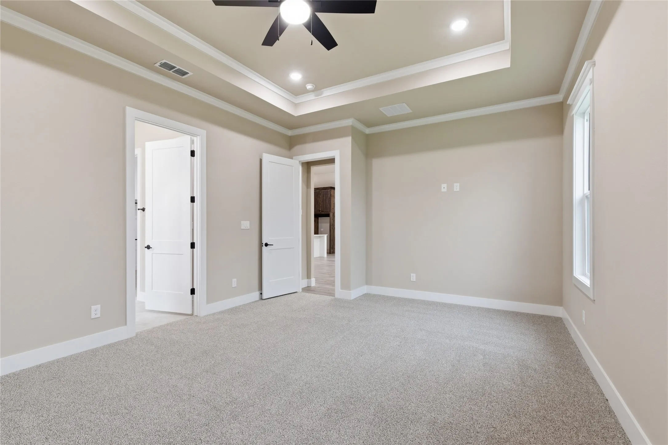 Spacious room featuring tray ceiling with recessed lighting and a ceiling fan, light-colored carpeting, and neutral wall paint