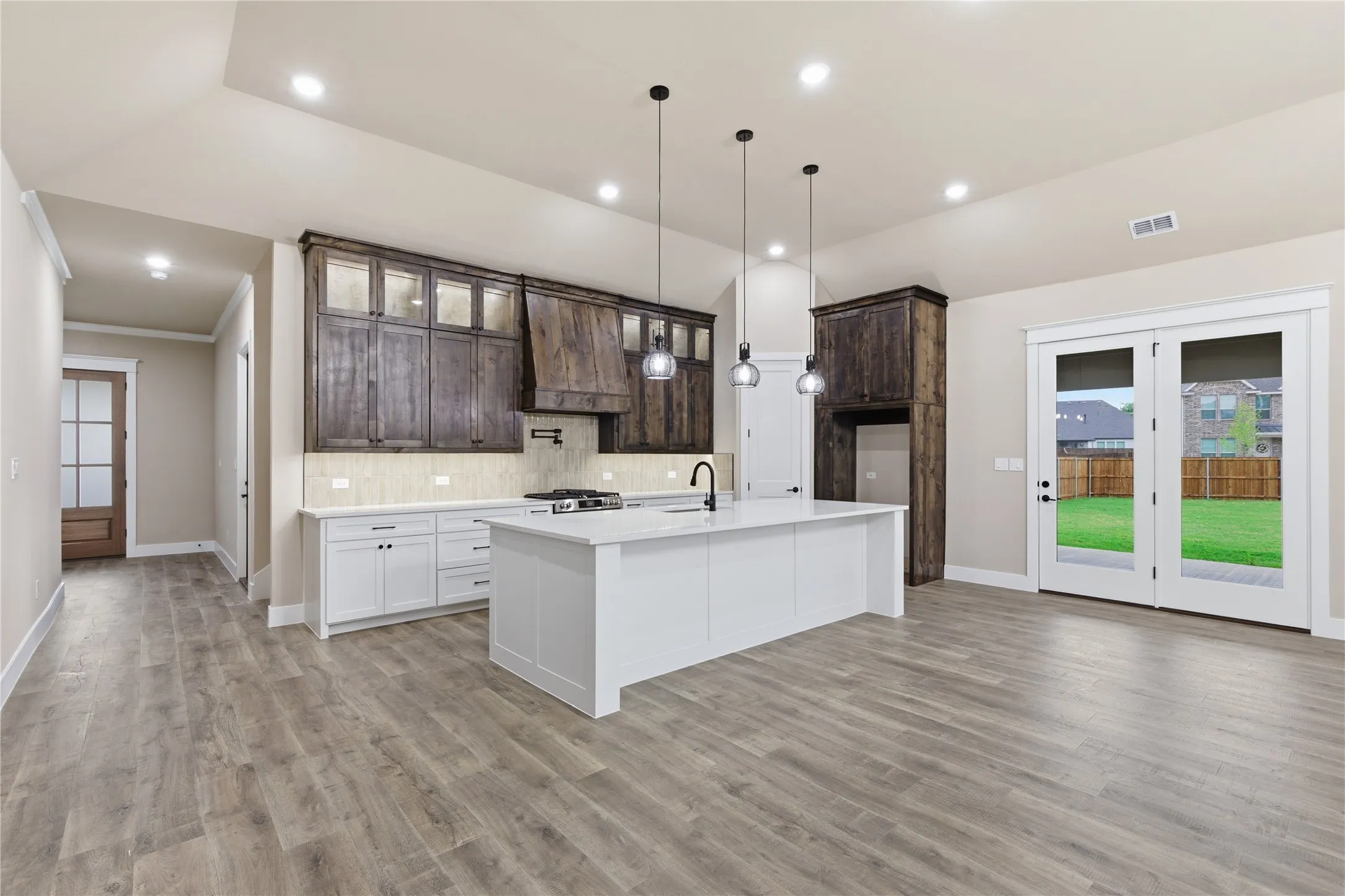 Open-concept kitchen featuring a large central island, two-tone cabinetry, wood-finish flooring, and double glass-paneled doors to the backyard