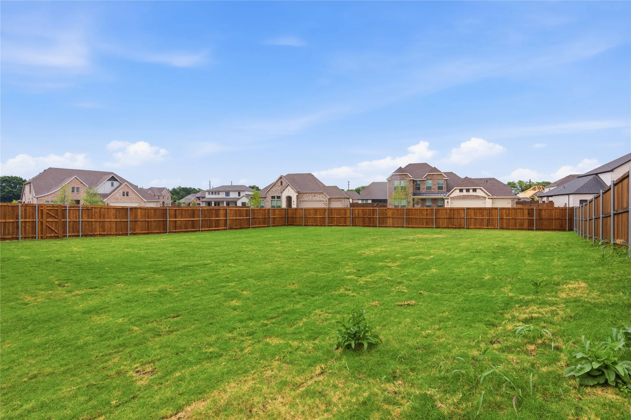 Expansive grassy yard area featuring a perimeter wood fence