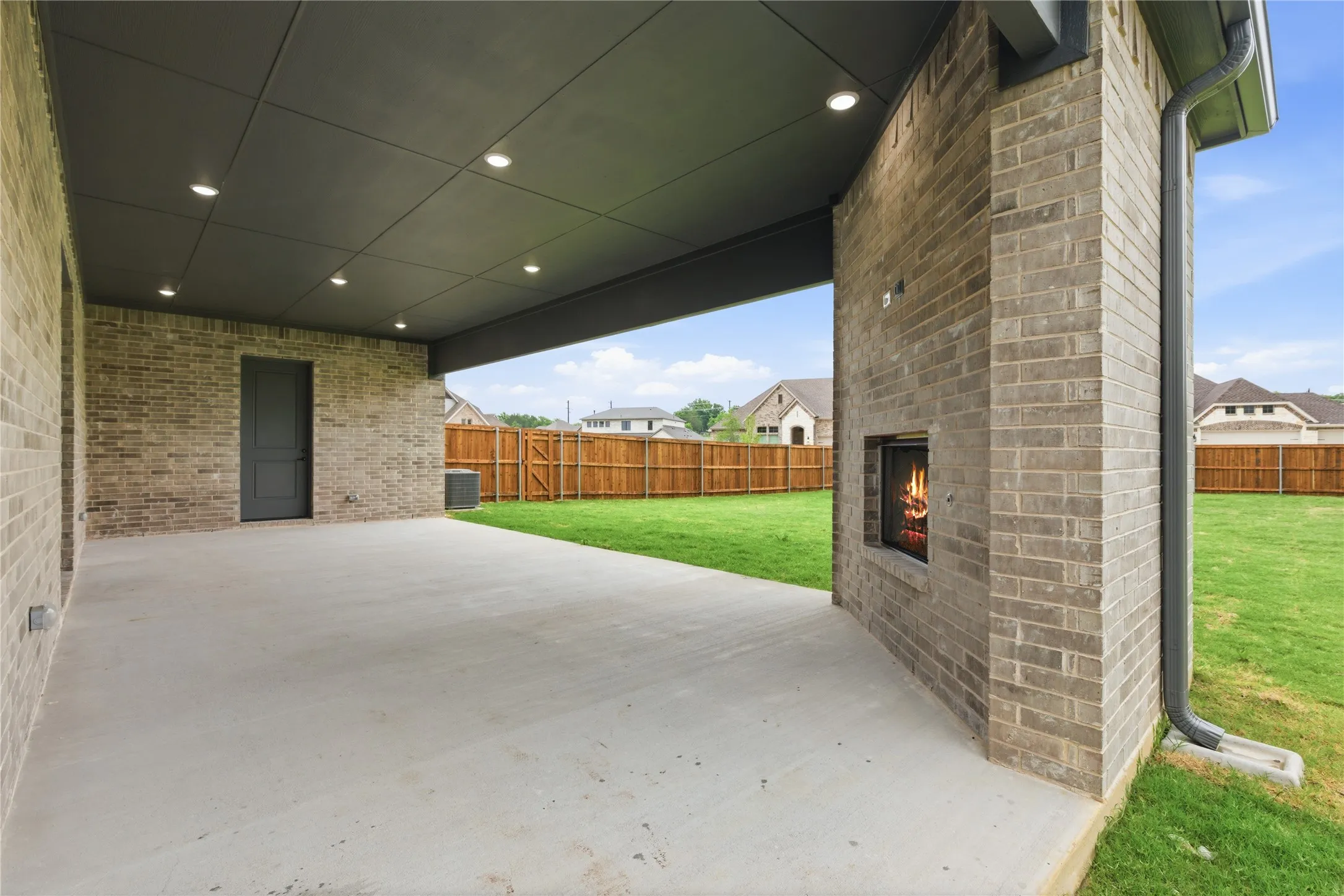 Expansive covered patio featuring a brick exterior with an outdoor fireplace, recessed lighting, and a grey plank ceiling