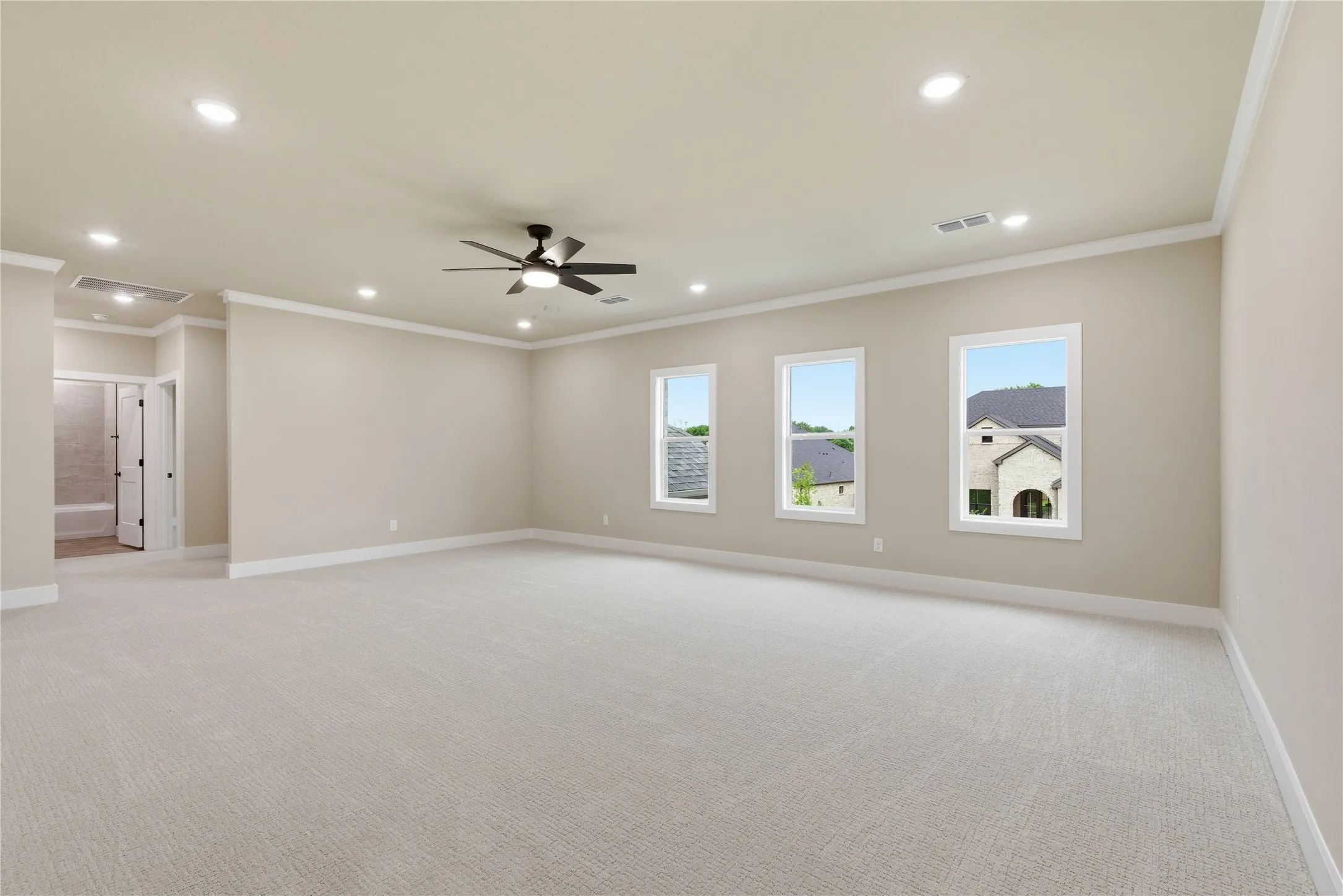 Spacious carpeted room featuring a ceiling fan, recessed lighting, crown molding, and three large windows