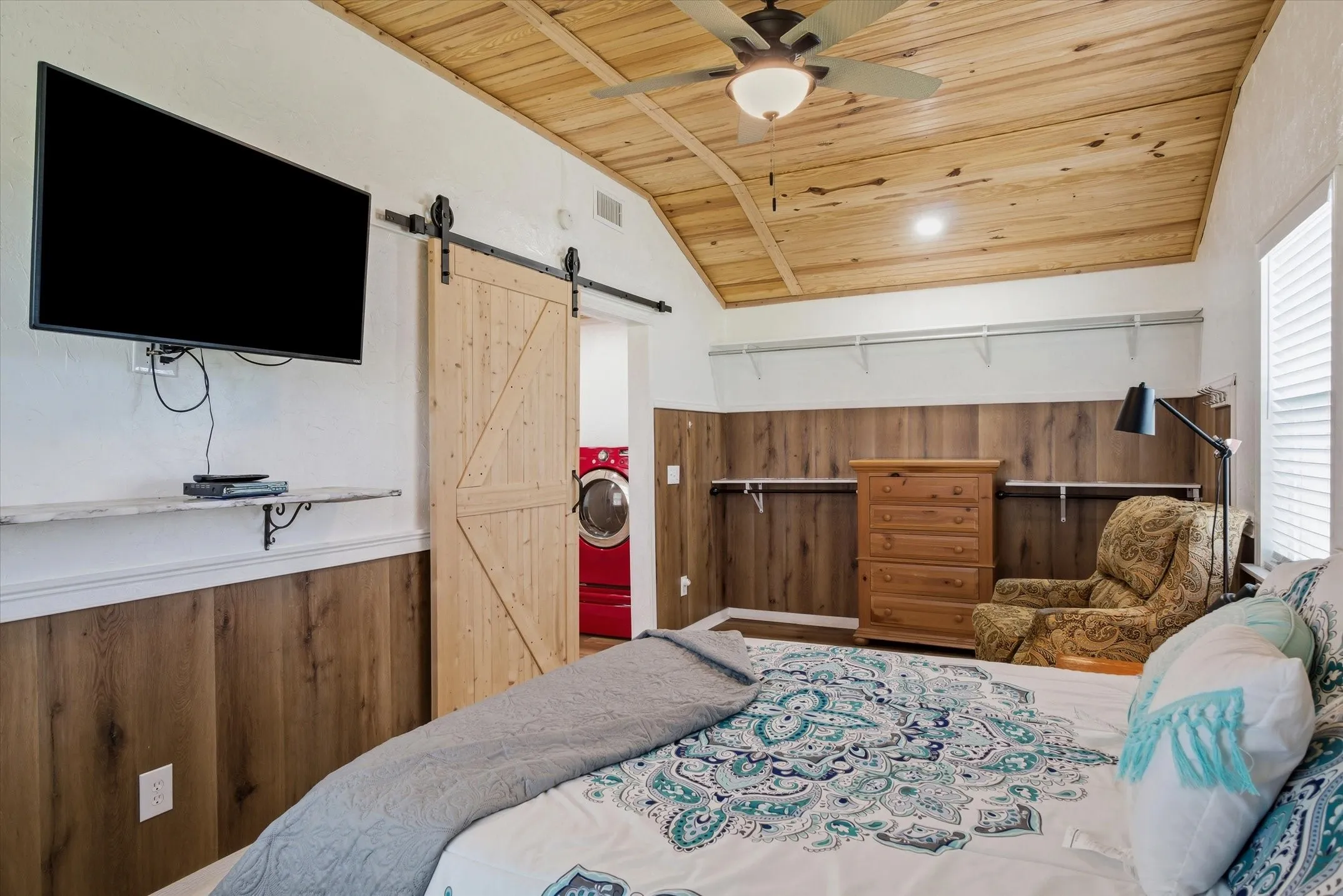 Bedroom with a vaulted wooden ceiling, a barn door, wooden walls, ceiling fan, and wainscoting