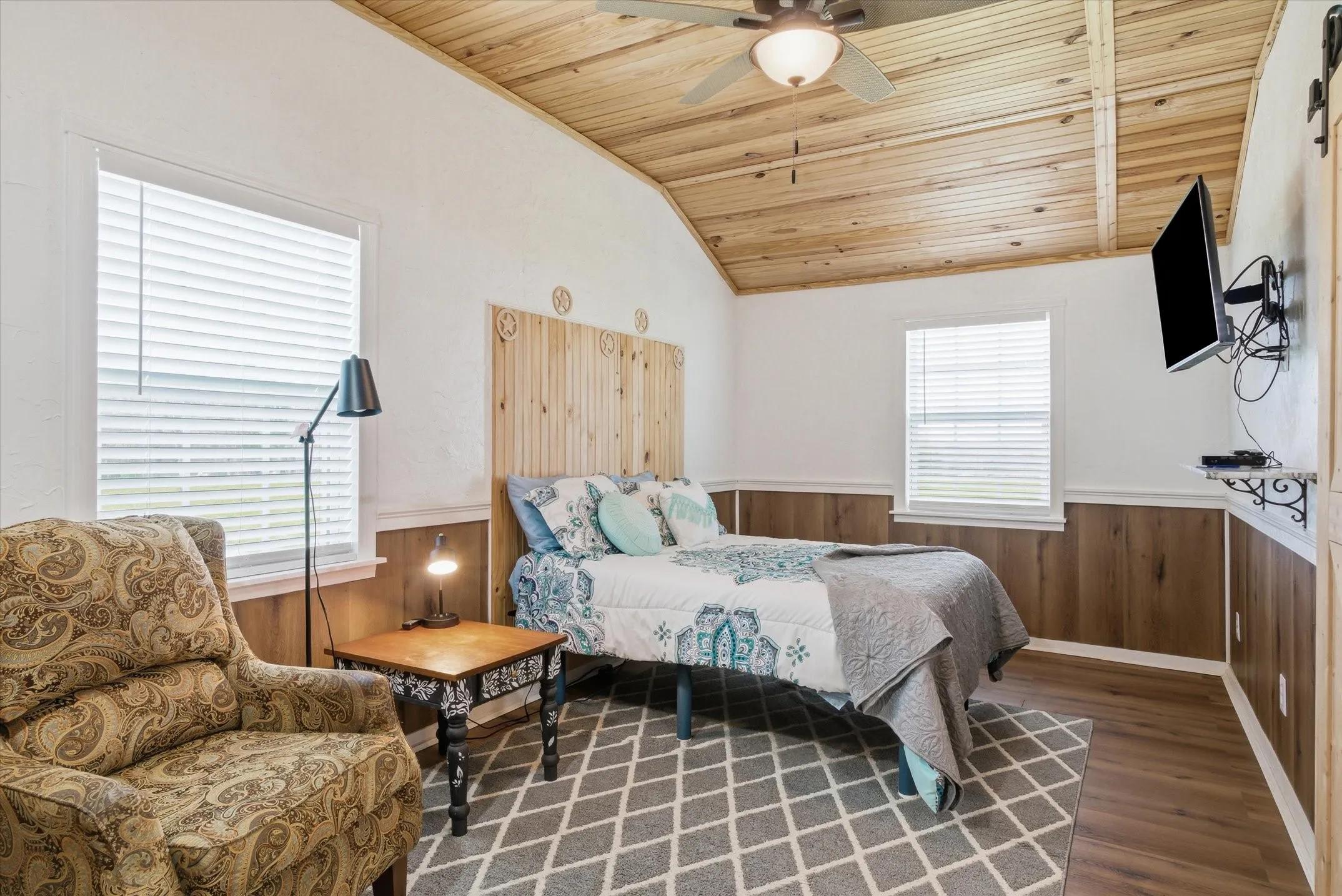 Bedroom with wooden walls, wood ceiling, wainscoting, ceiling fan, and dark wood-style floors