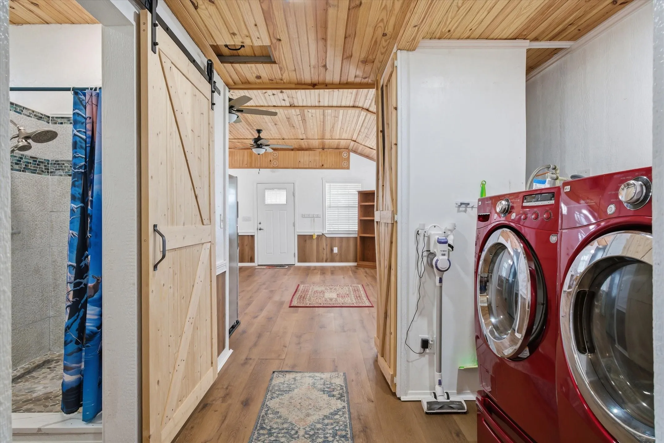 Laundry area featuring a vaulted wooden ceiling, a barn door, light wood-style flooring, wood walls, and a ceiling fan