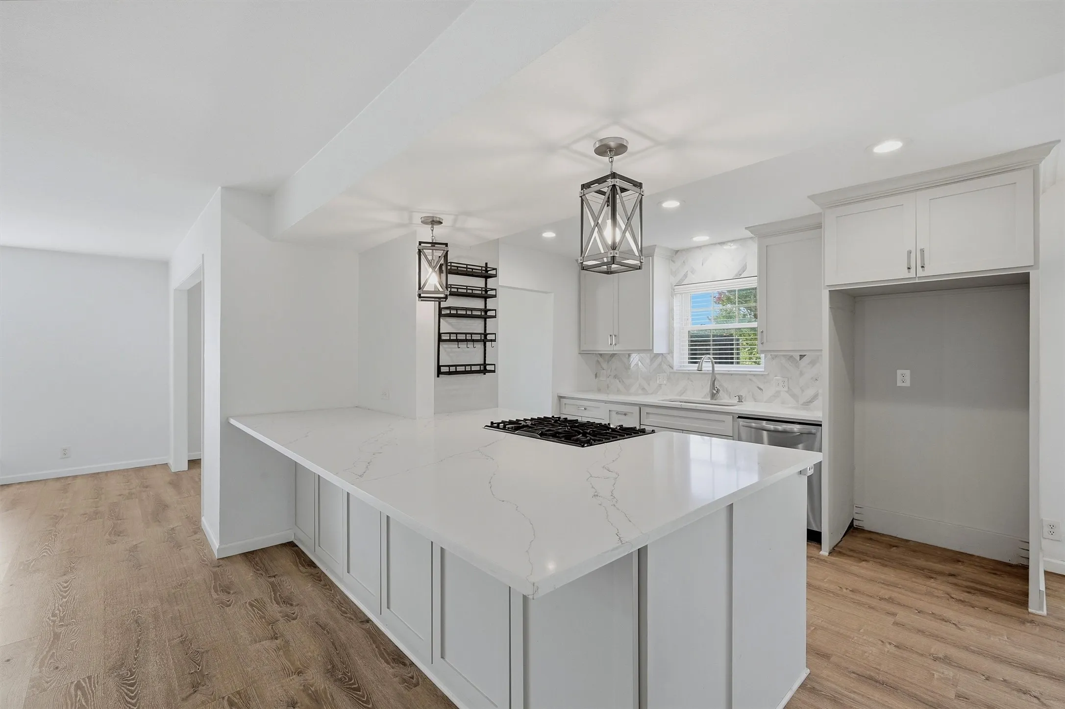 Kitchen featuring a large island with cooktop, stone countertops, white shaker cabinetry, stainless steel dishwasher, and wood-finish flooring