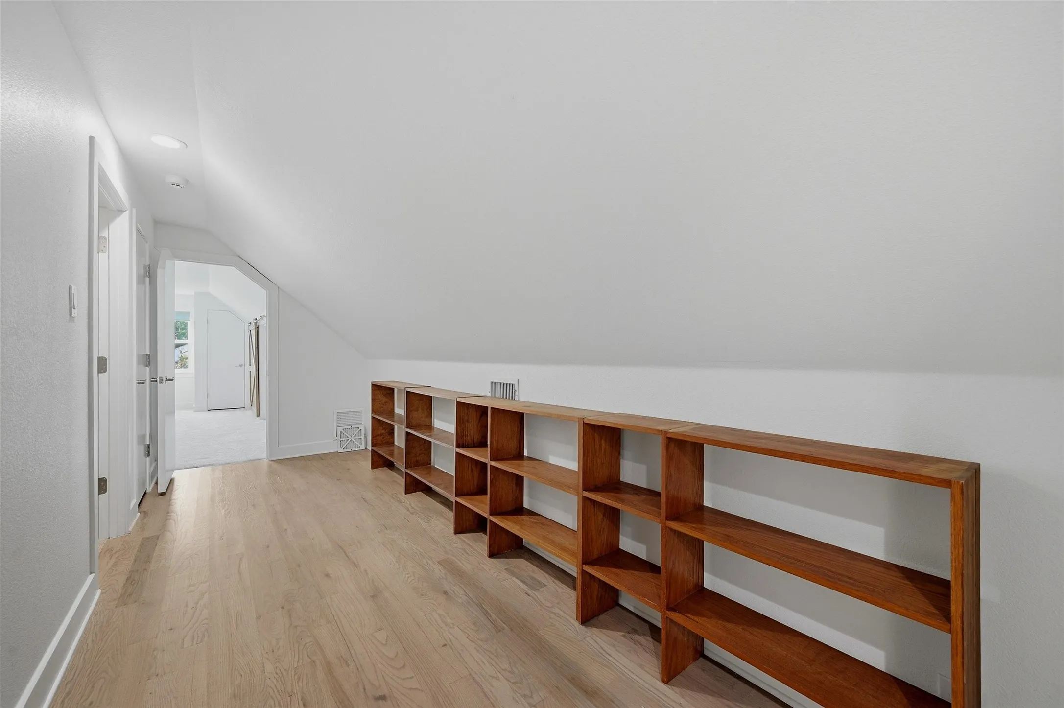 Sloped ceiling hallway featuring wood-finish flooring, recessed lighting, and built-in shelving