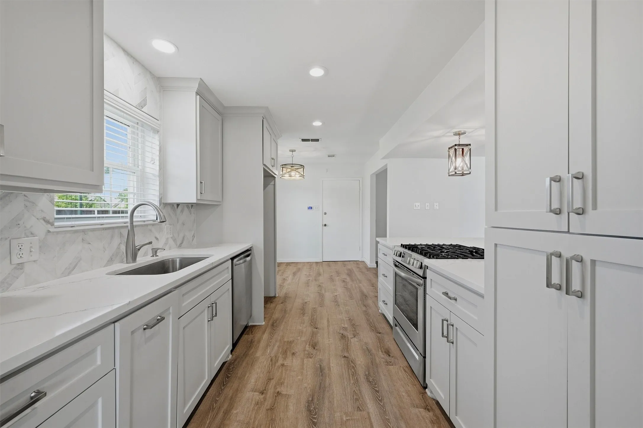 Galley kitchen featuring white cabinetry, light-toned countertops, a stainless steel gas range, and wood-finish flooring