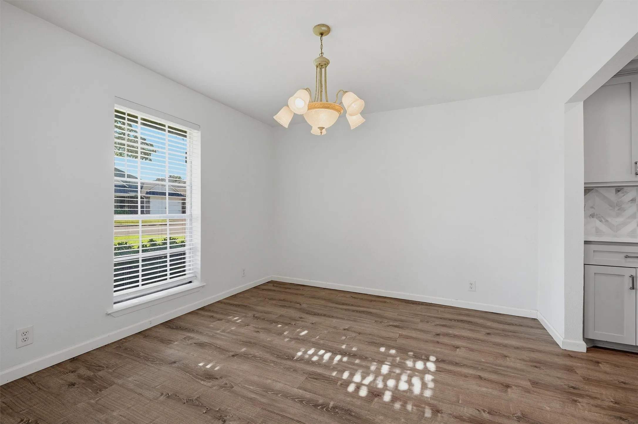 Wood-finish flooring, white walls, and a multi-arm chandelier create a bright interior