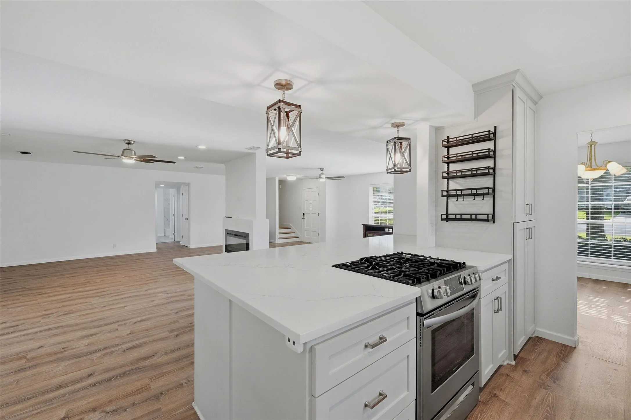 Kitchen island with integrated stainless steel range, white shaker-style cabinetry, white countertops, and wood-finish flooring