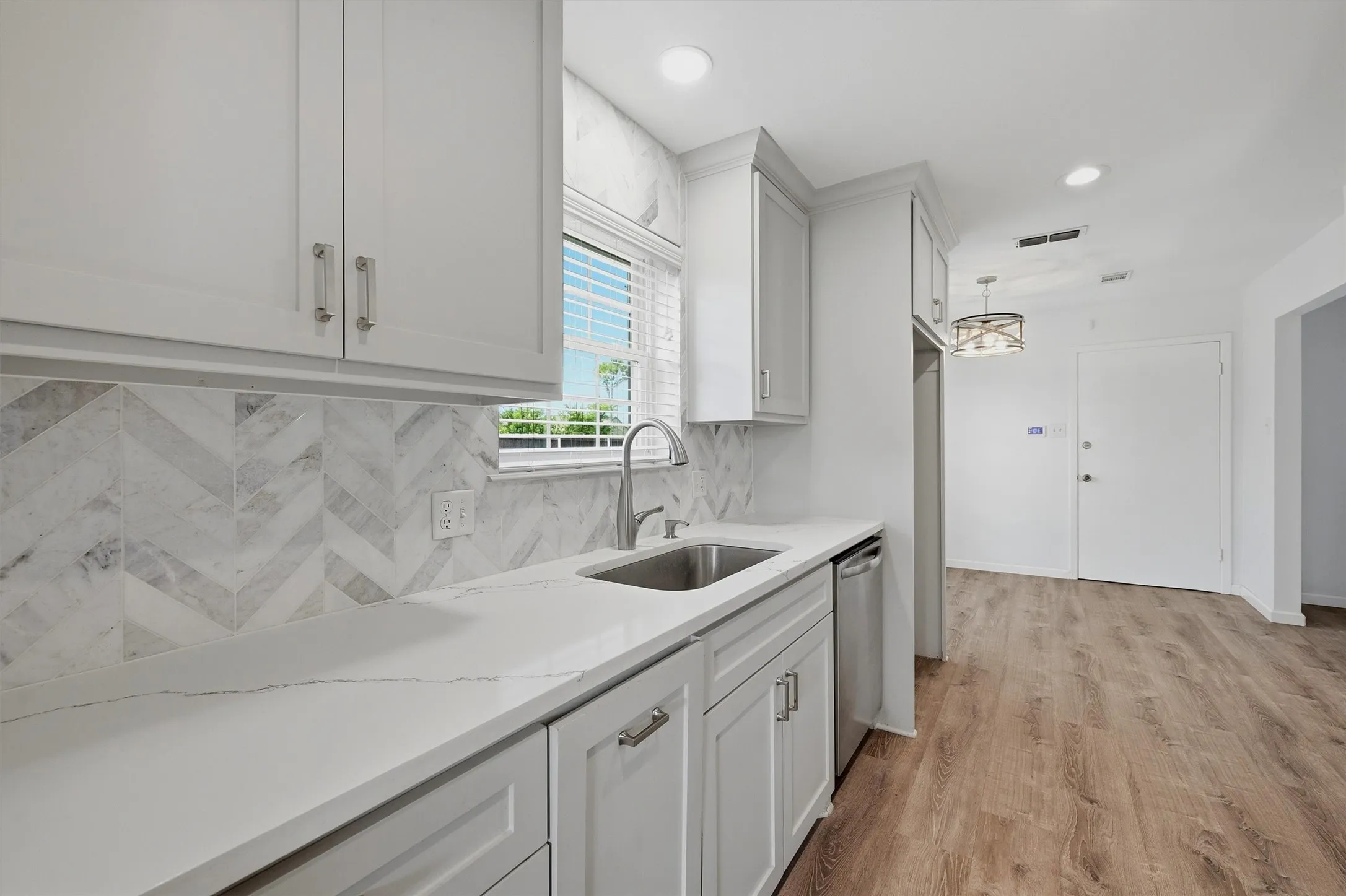 Kitchen featuring white shaker cabinetry, white countertop, herringbone tile backsplash, stainless steel sink, and wood-finish flooring