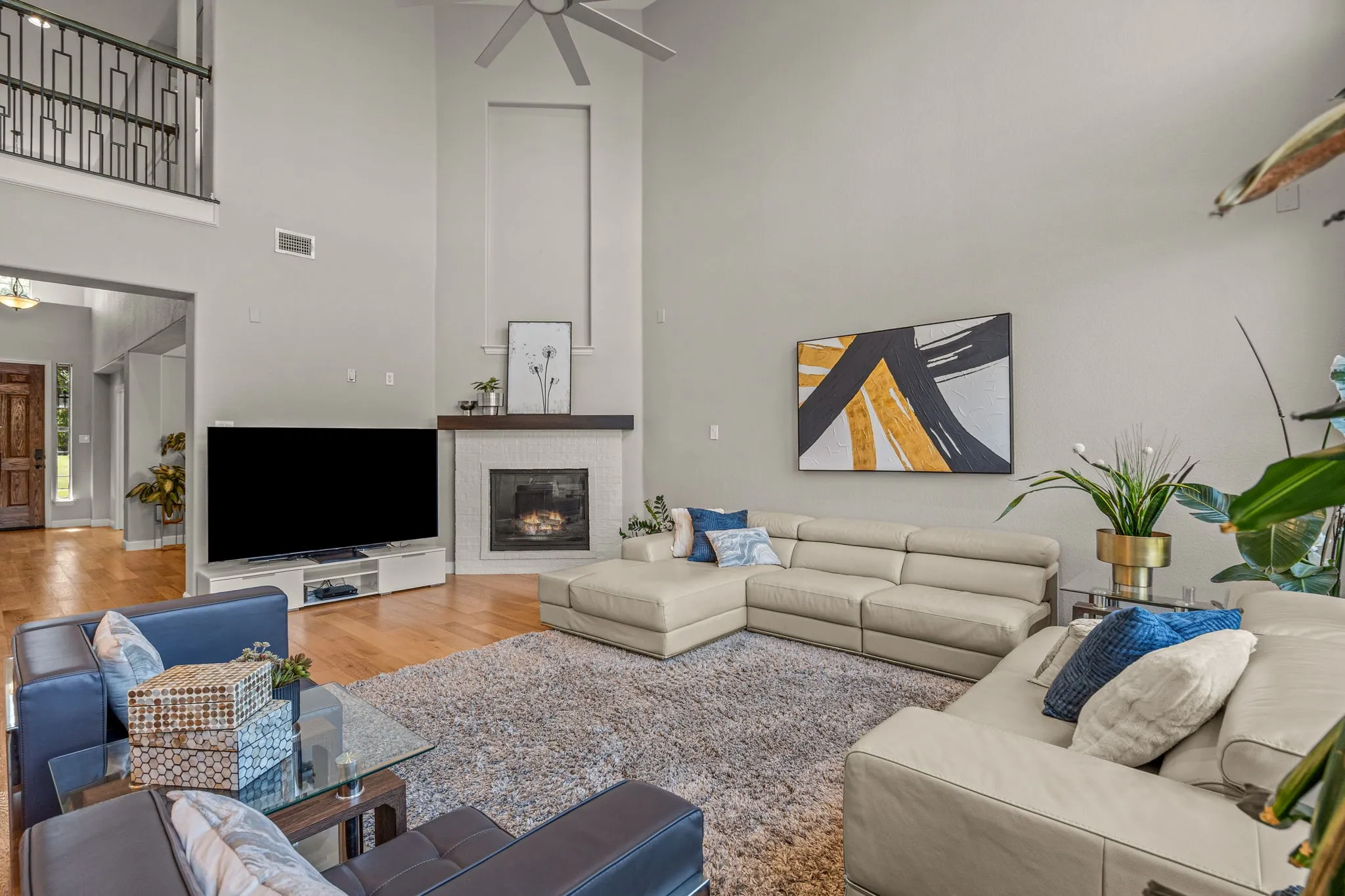 Living room with a high ceiling, wood finished floors, a ceiling fan, and a brick fireplace