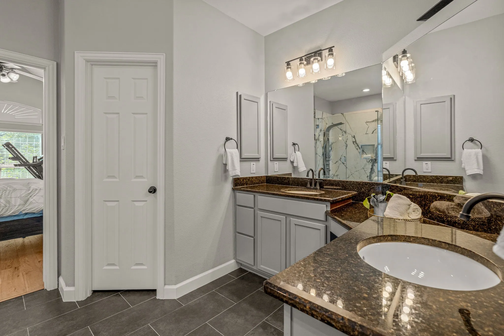 Ensuite bathroom featuring double vanity, two vanities, a marble finish shower, and dark tile patterned flooring