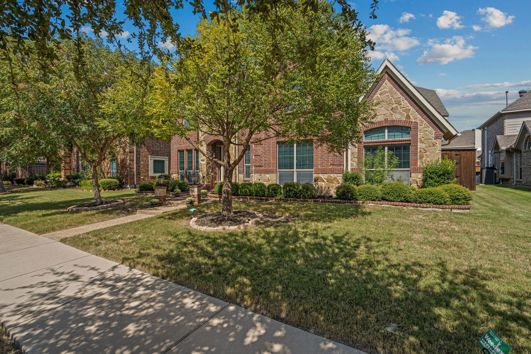 View of property hidden behind natural elements featuring stone siding and a front lawn