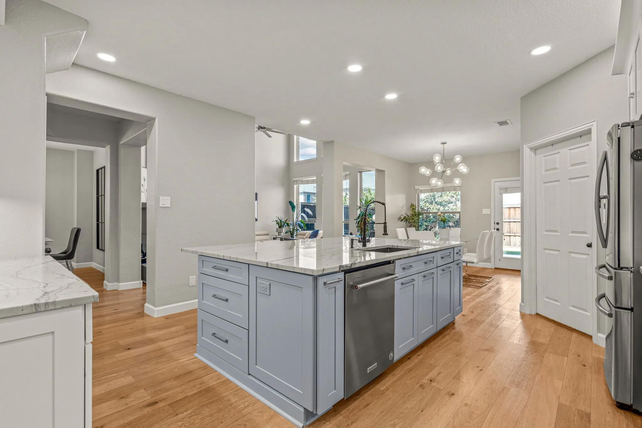 Kitchen with light stone counters, gray cabinets, a center island with sink, and light wood-style floors