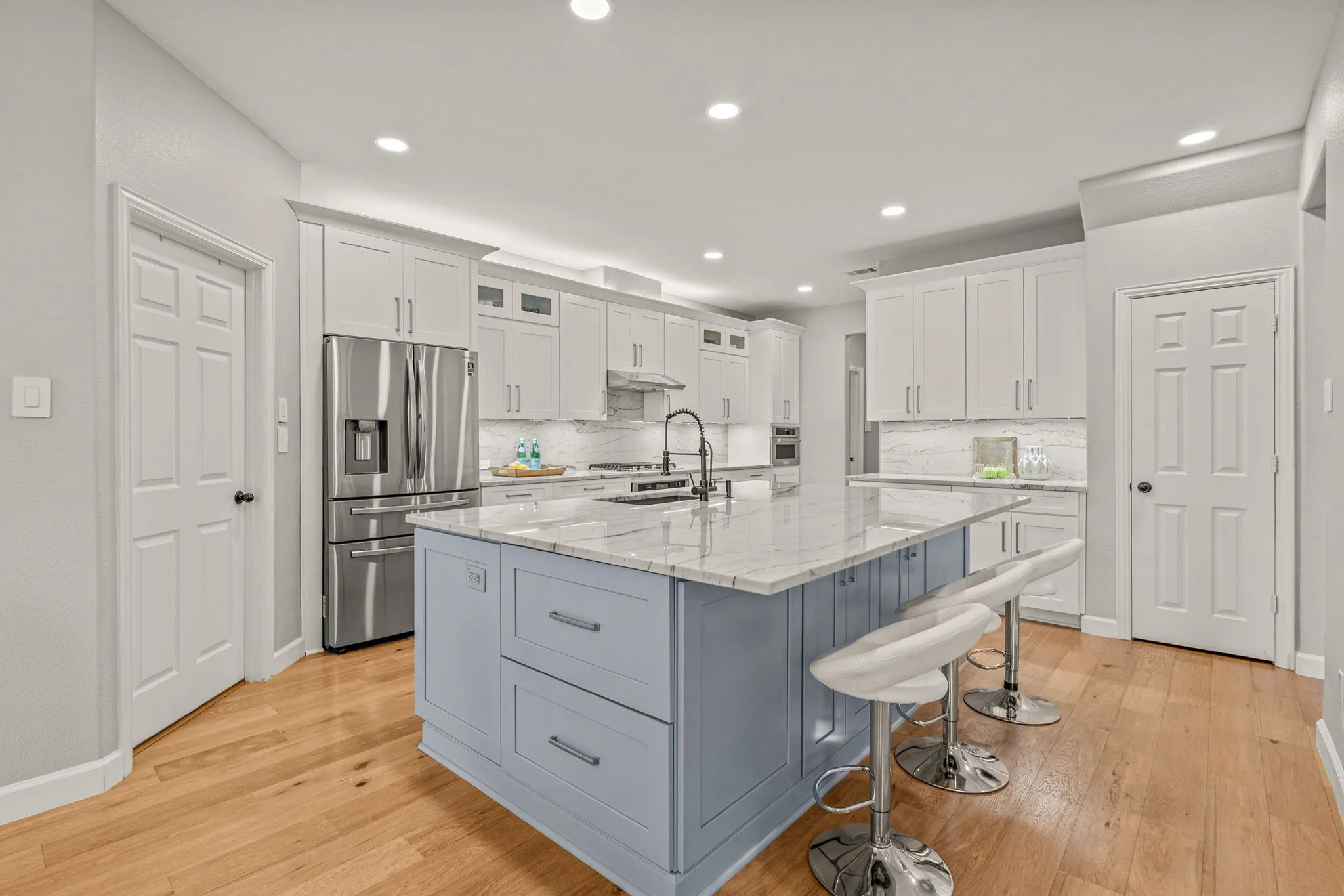 Kitchen featuring stainless steel appliances, light stone counters, glass insert cabinets, an island with sink, and a kitchen breakfast bar