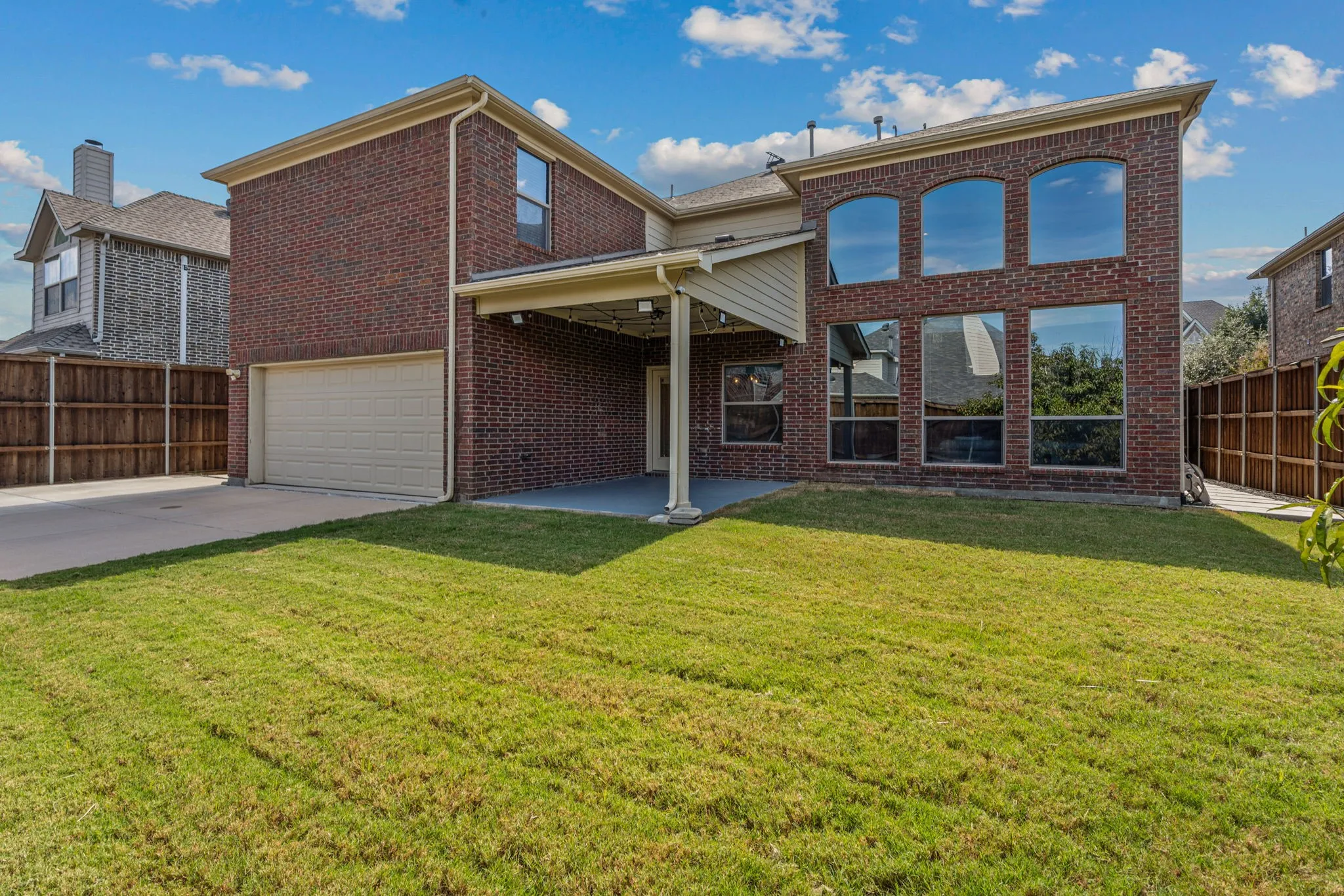 Rear view of property featuring a fenced backyard, brick siding, a garage, a patio area, and concrete driveway