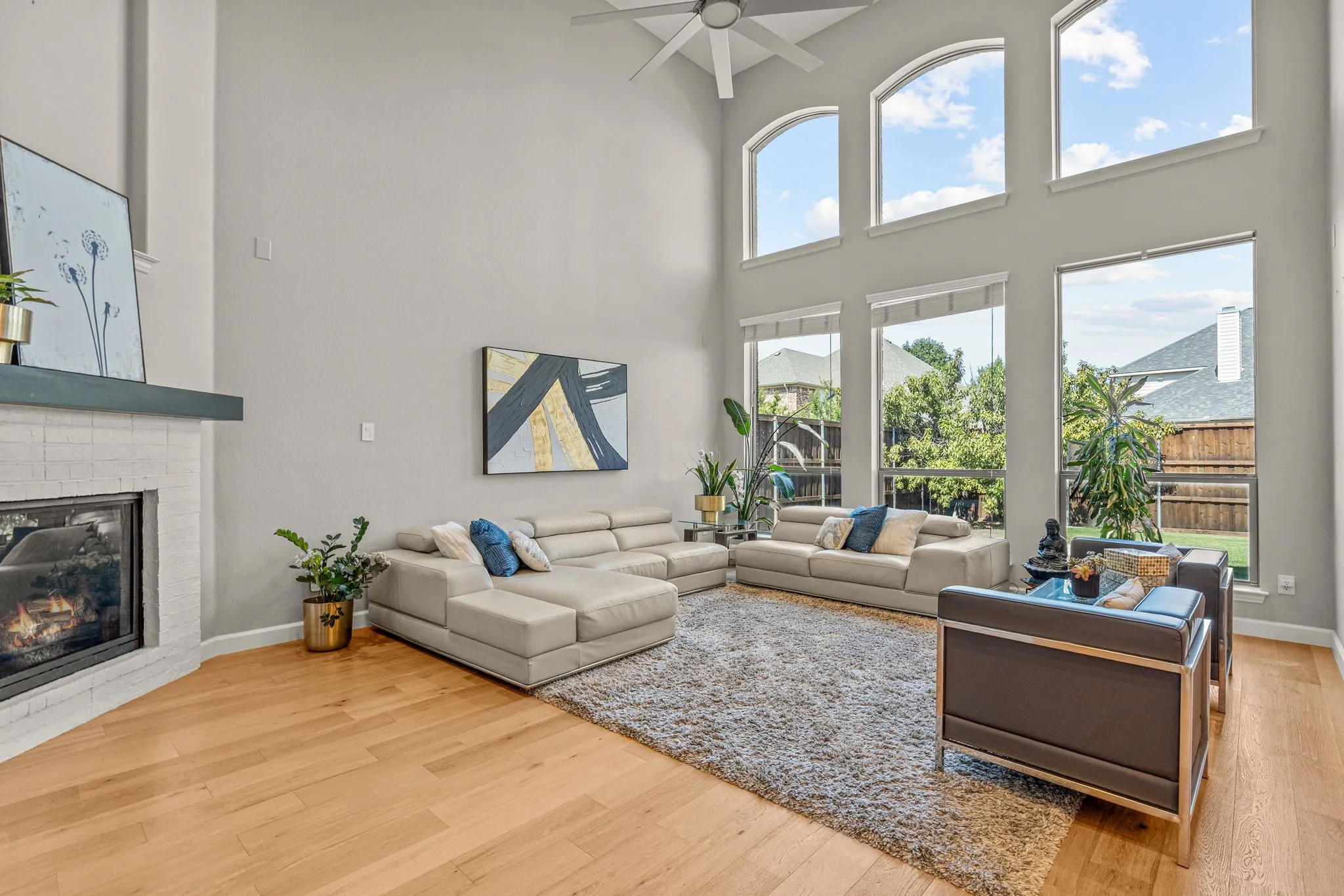 Living room with light wood-style floors, ceiling fan, a brick fireplace, and a high ceiling