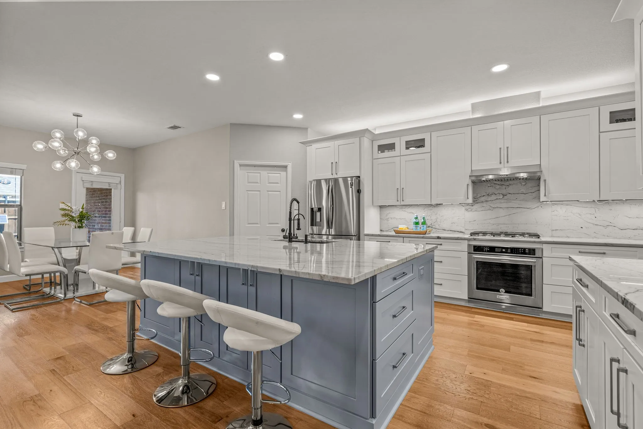 Dual tone kitchen with light stone countertops, a kitchen island with sink, a kitchen bar, stainless steel appliances, and light wood finished floors