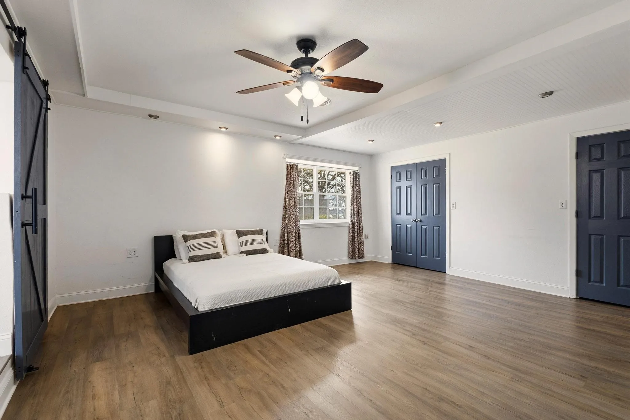 Bedroom with a barn door, dark wood finished floors, and ceiling fan