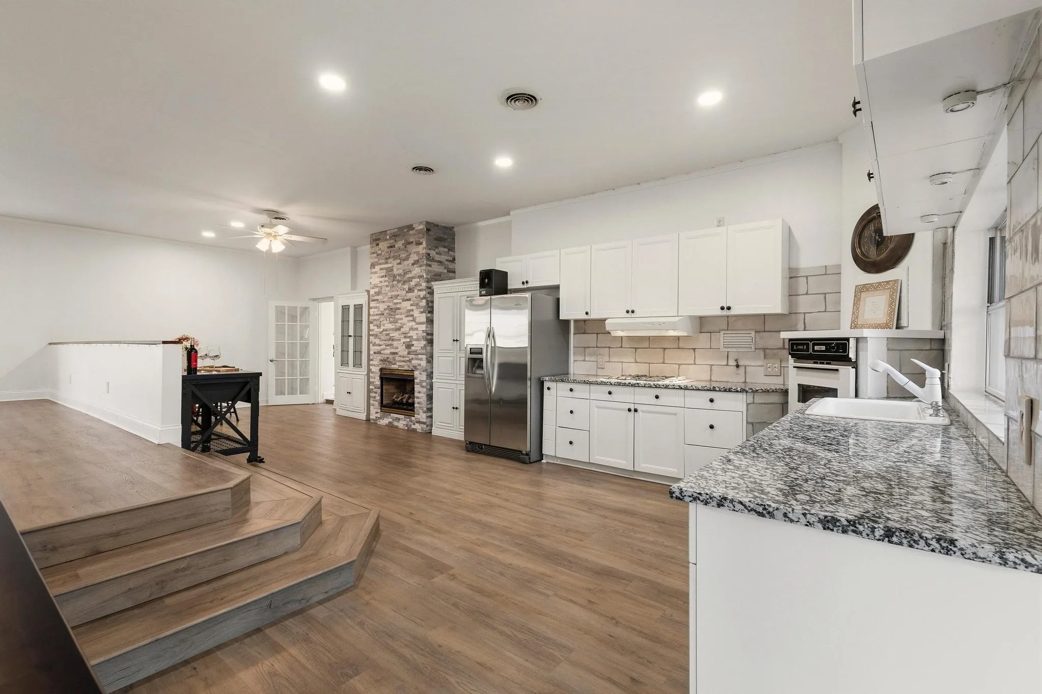 Kitchen featuring a stone fireplace, white cabinets, stainless steel fridge with ice dispenser, dark stone countertops, and dark wood finished floors