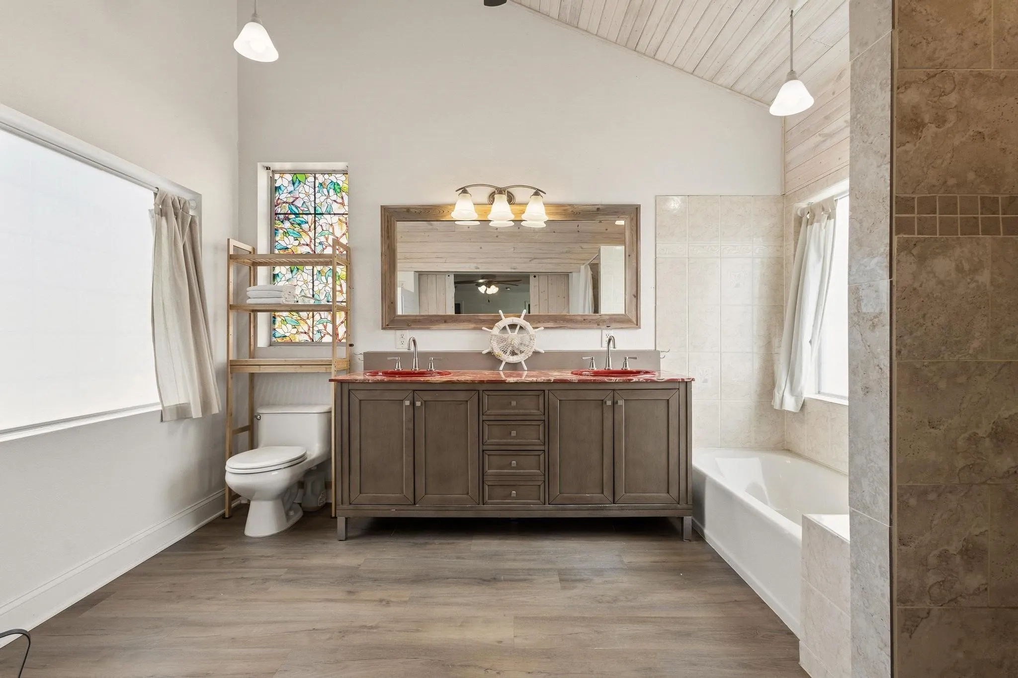 Primary ensuite bathroom featuring double vanity, light wood-type flooring, a bath, and vaulted ceiling