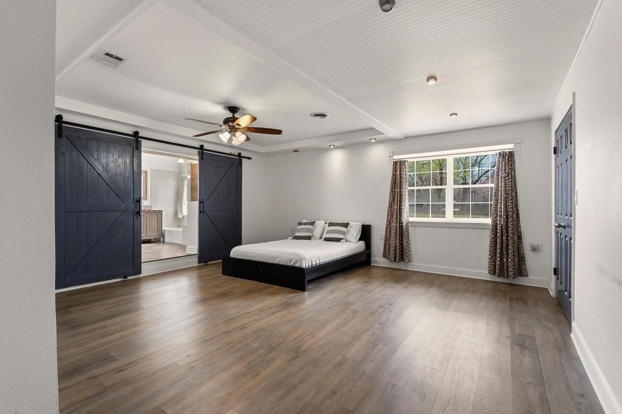 Bedroom with a barn door, dark wood-style flooring, a ceiling fan, and connected bathroom