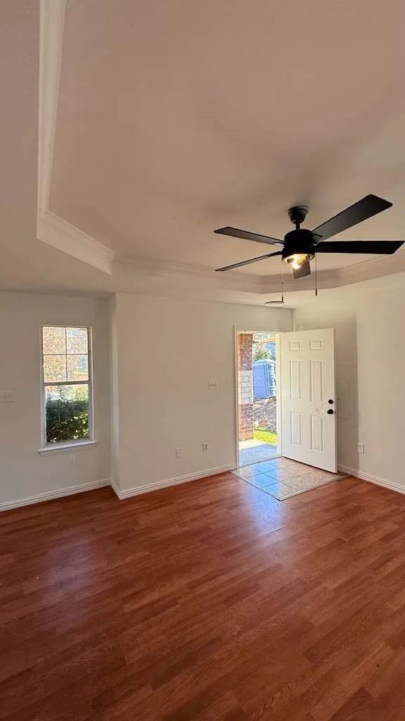 Empty room with dark wood-style flooring, ceiling fan, and a raised ceiling