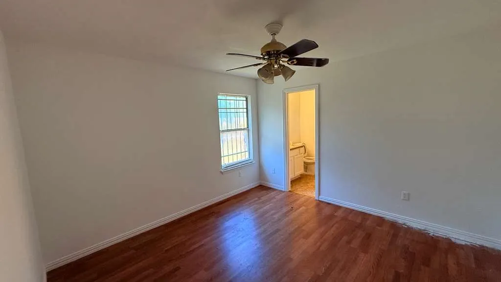 Unfurnished bedroom with dark wood-style floors, ceiling fan, and ensuite bath