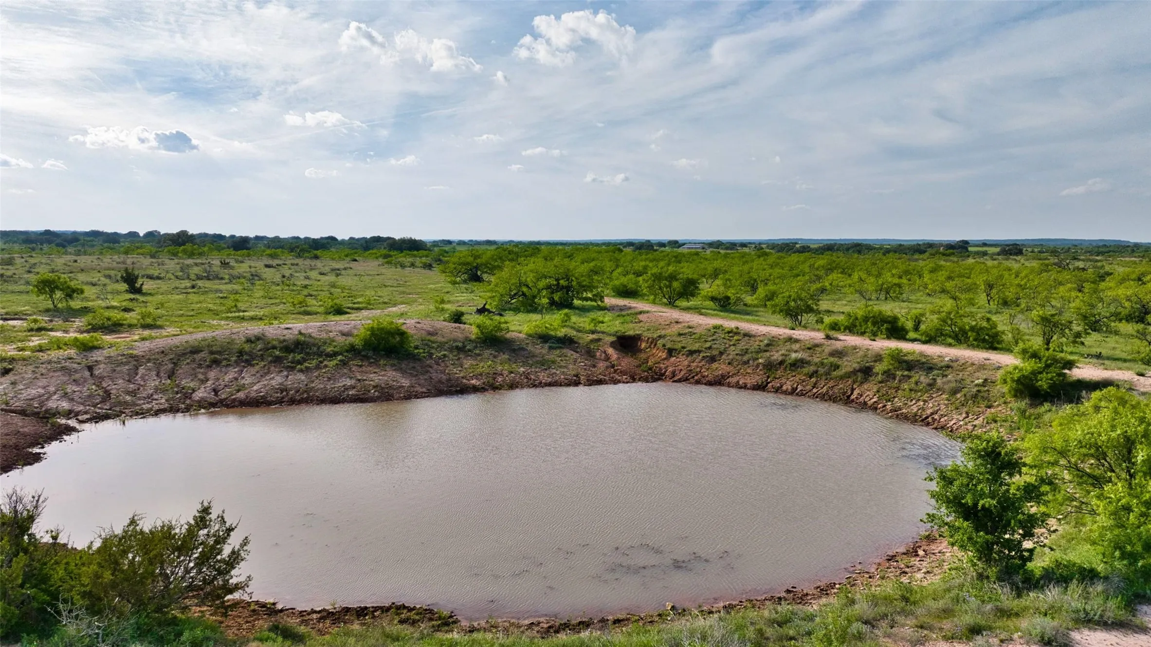 Expansive land featuring a large pond and a winding dirt road