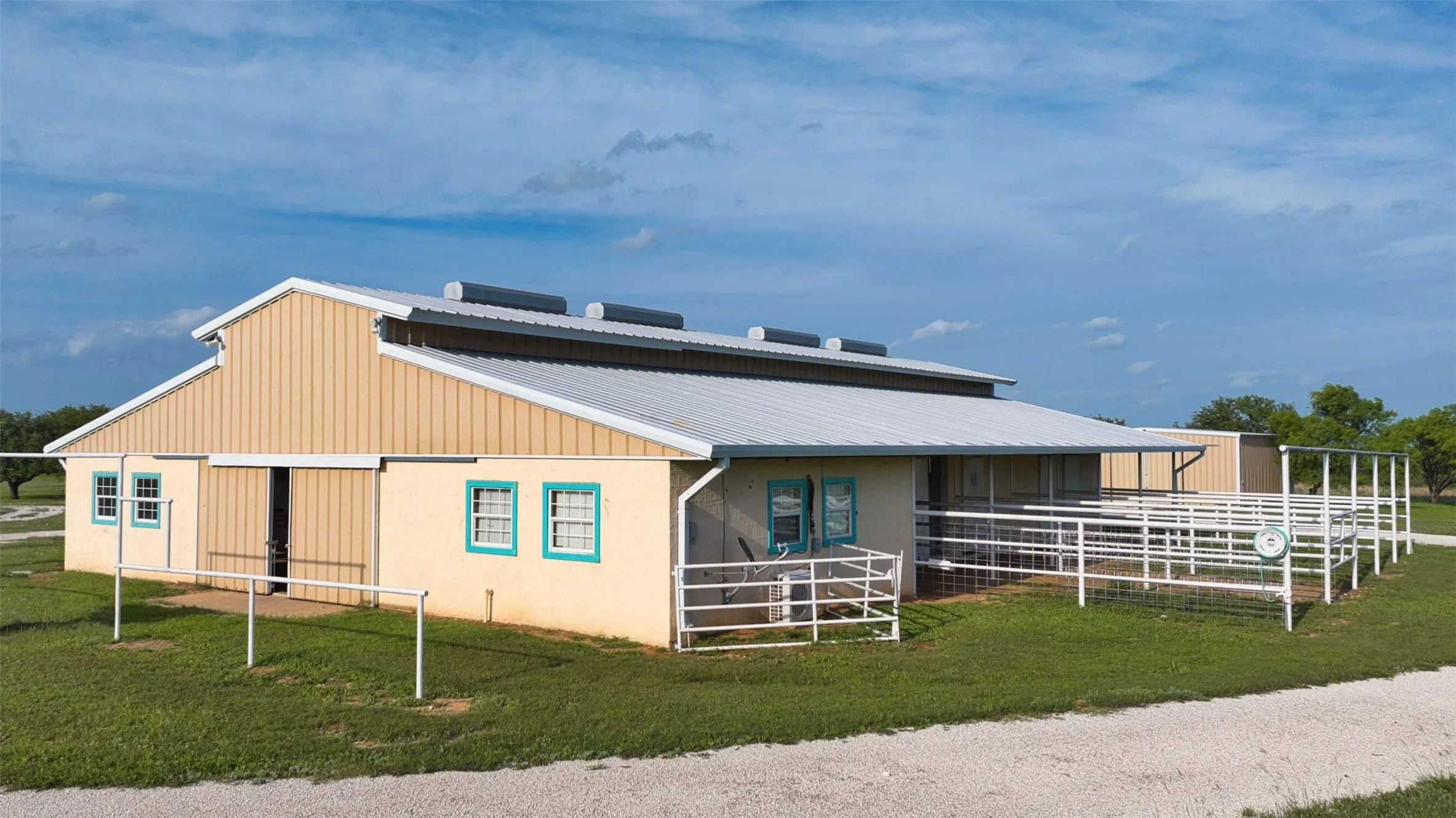 Metal-roofed barn with a cream-colored exterior and teal window trim
