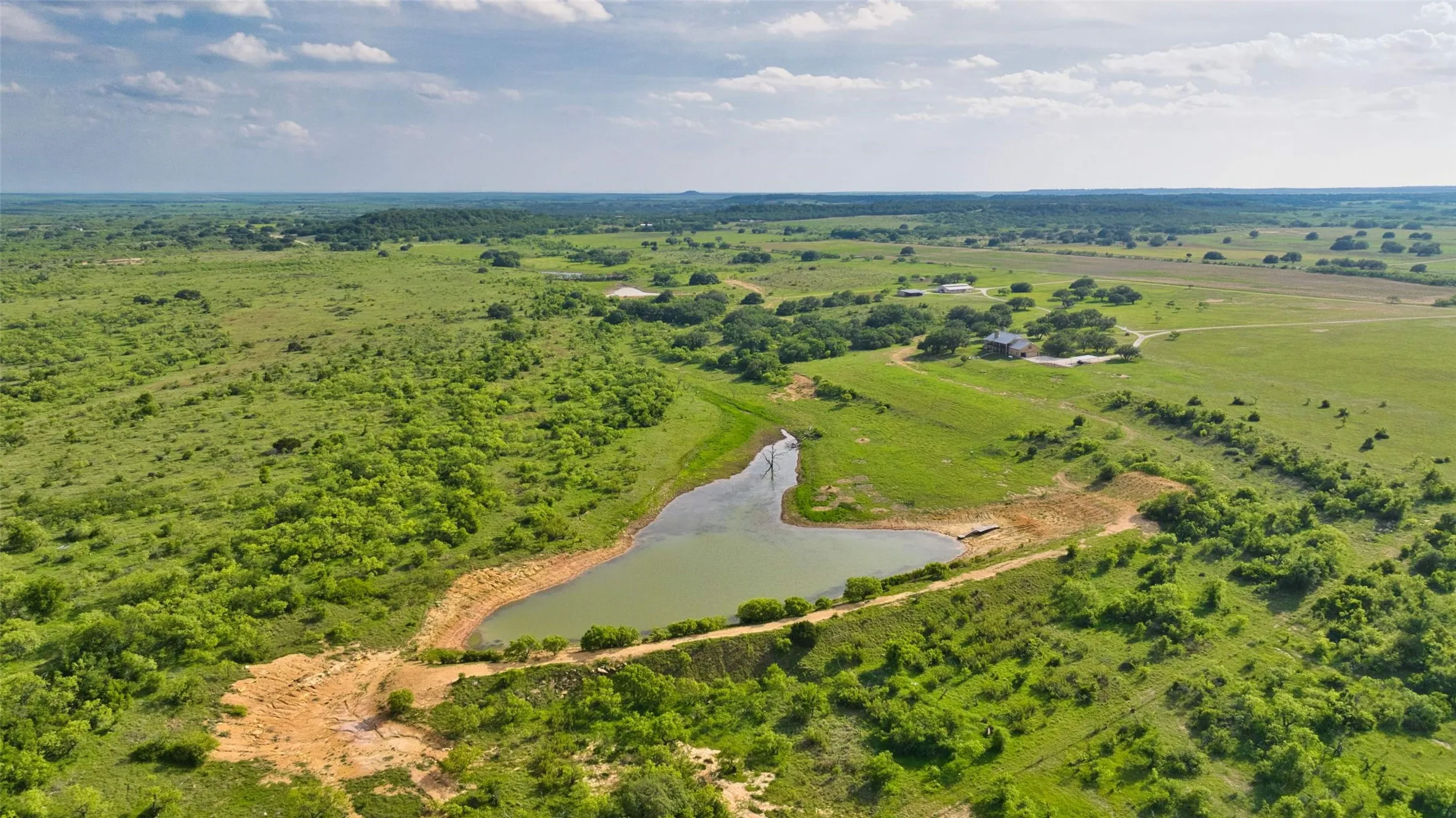 Expansive rural landscape featuring a private pond, open pastures, scattered mature trees, and a distant residence
