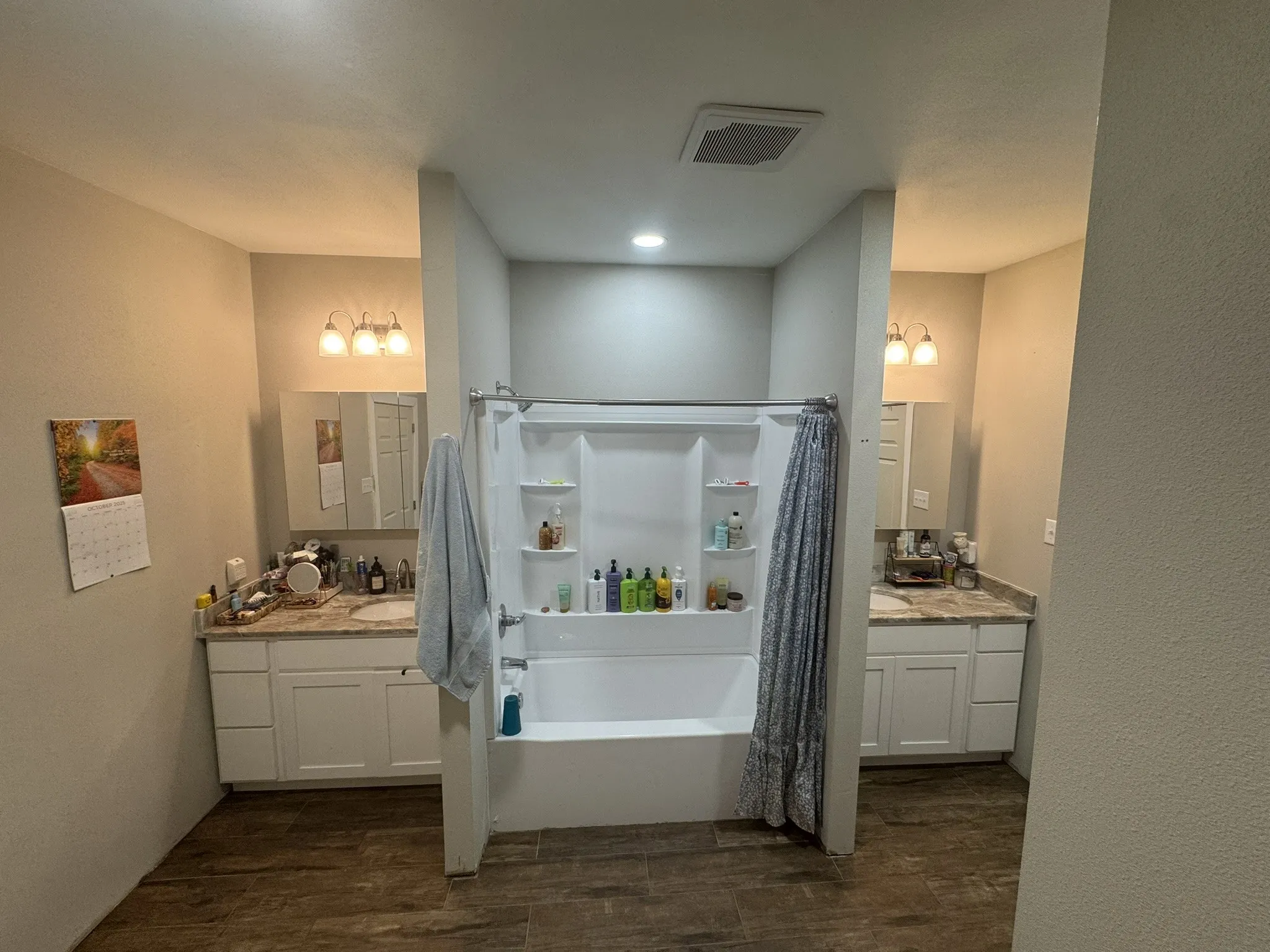 Bathroom featuring two vanities, dark wood-style floors, a textured wall, and shower / bath combo