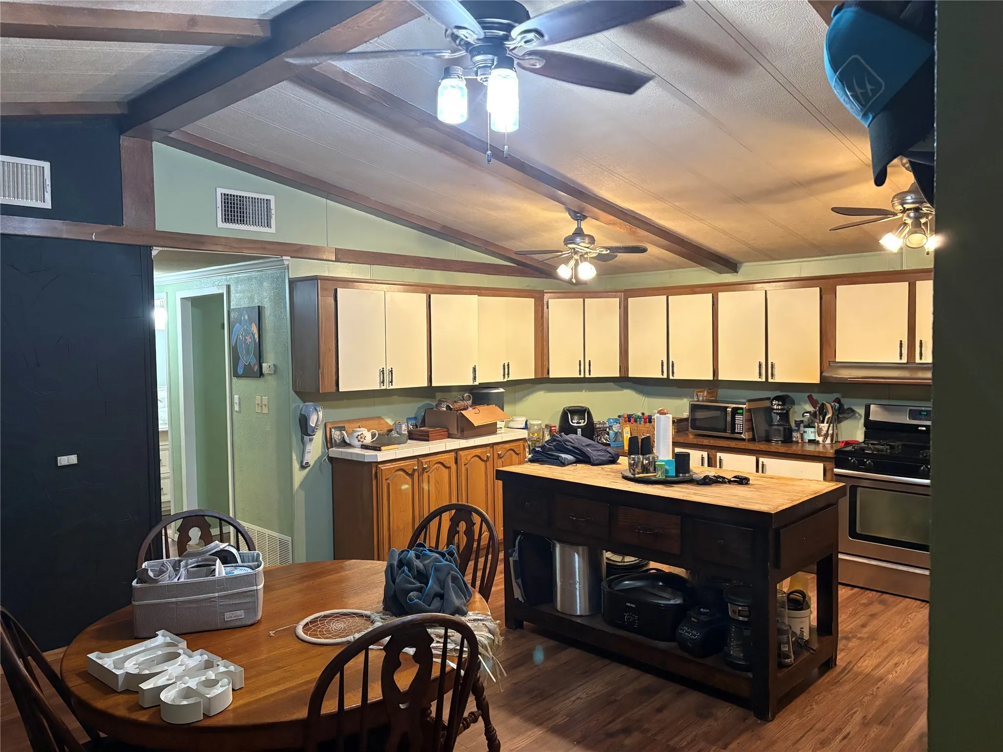 Two tone kitchen featuring beamed ceiling, stainless steel appliances, dark wood-style flooring, and two tone color scheme