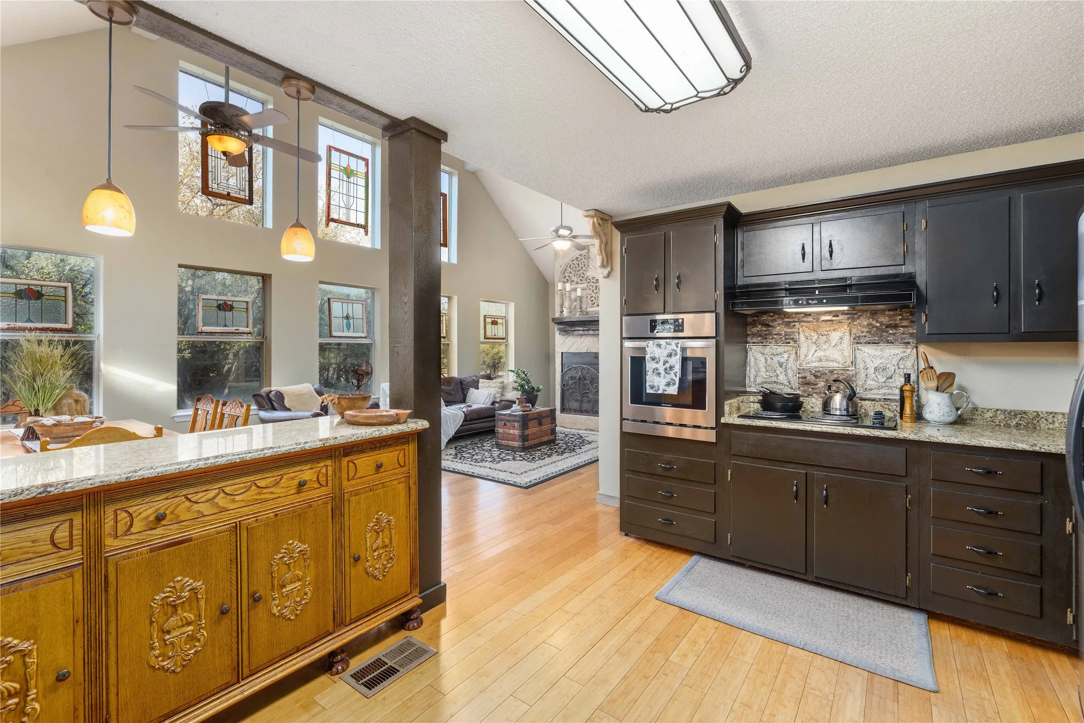 Kitchen with ceiling fan, stainless steel oven, light stone countertops, a large fireplace, and light wood-style floors