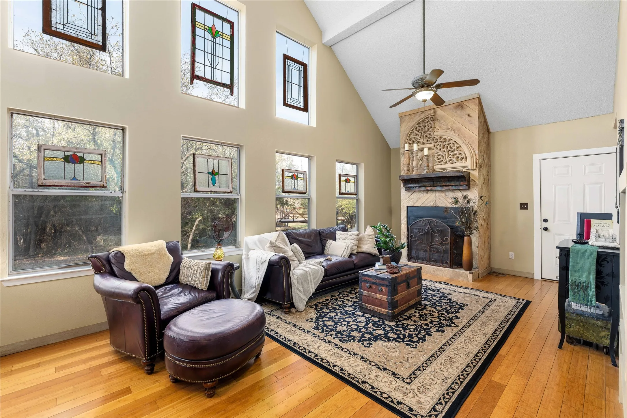 Living area featuring light wood finished floors, ceiling fan, a large fireplace, and vaulted ceiling