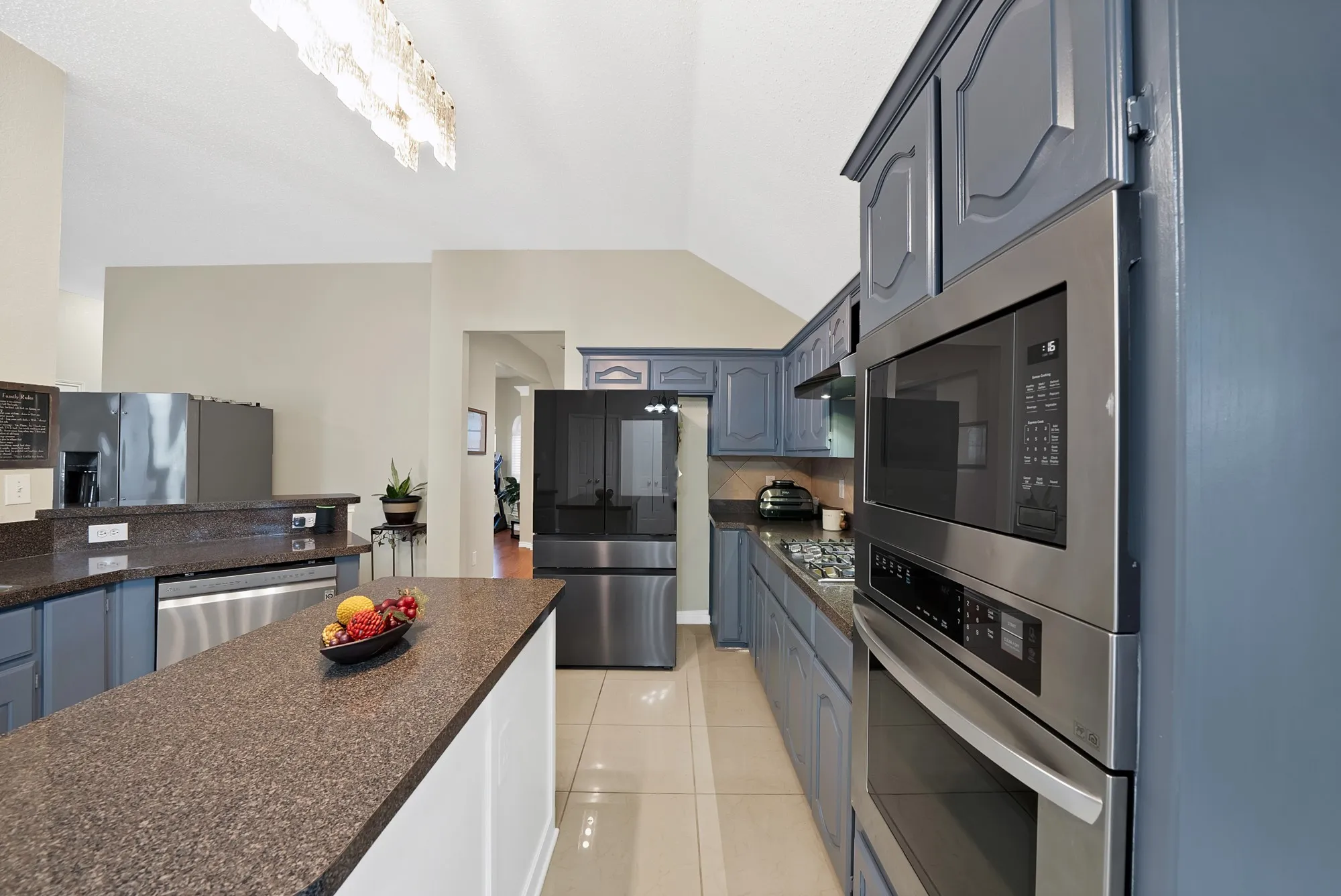 Kitchen with stainless steel appliances, vaulted ceiling, light tile patterned floors, backsplash, and blue cabinets