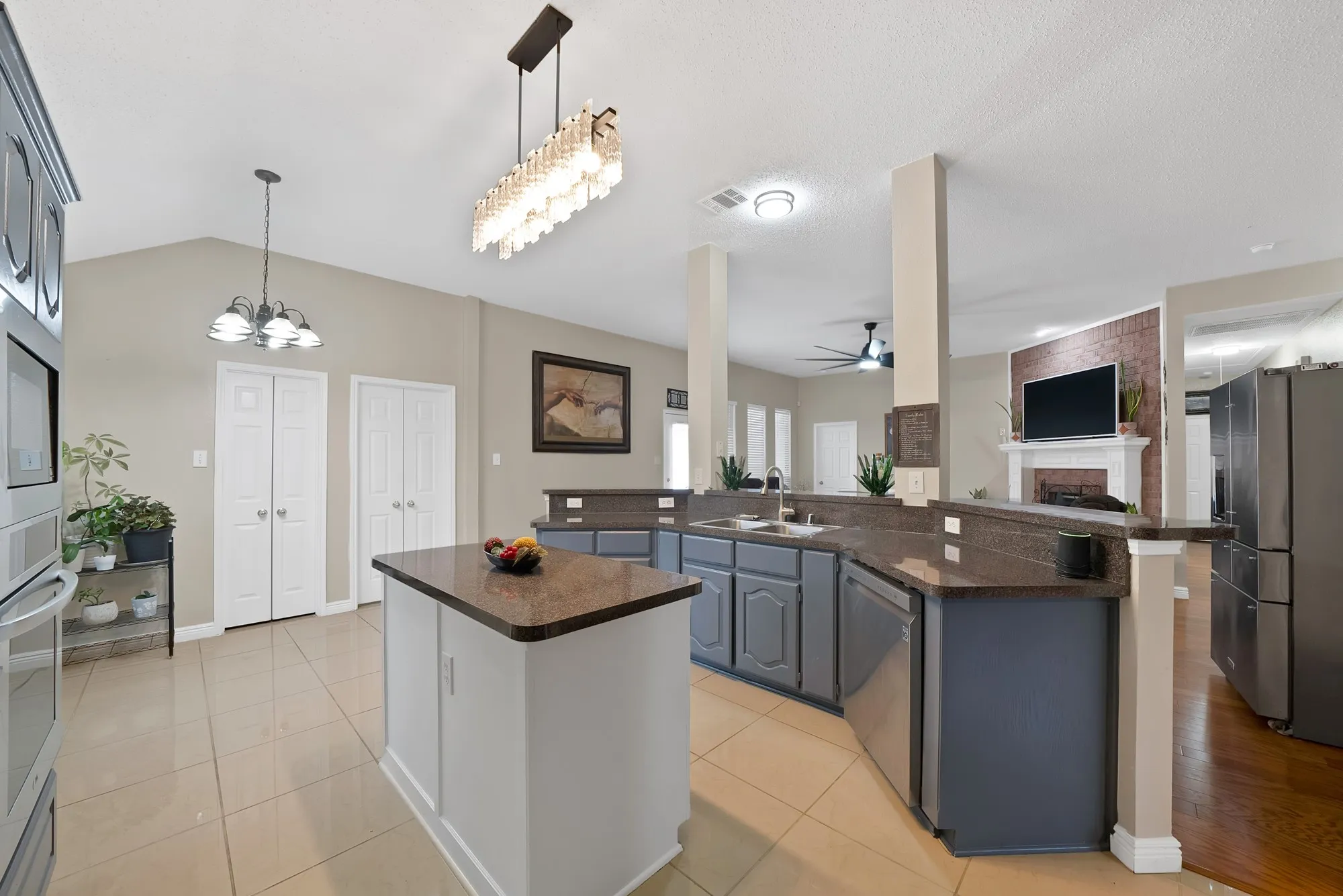 Kitchen featuring open floor plan, stainless steel appliances, a fireplace, light tile patterned floors, and lofted ceiling