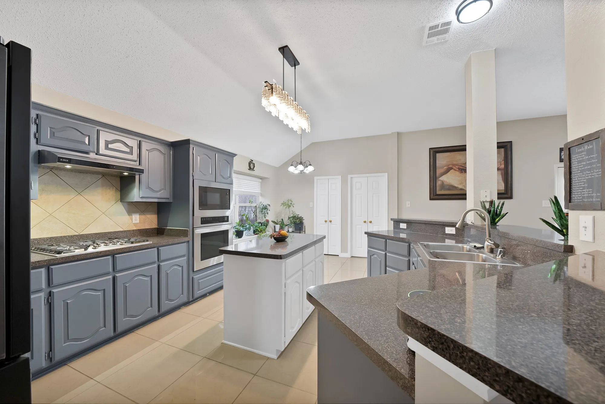 Kitchen featuring gray cabinets, light tile patterned flooring, stainless steel appliances, and hanging lights