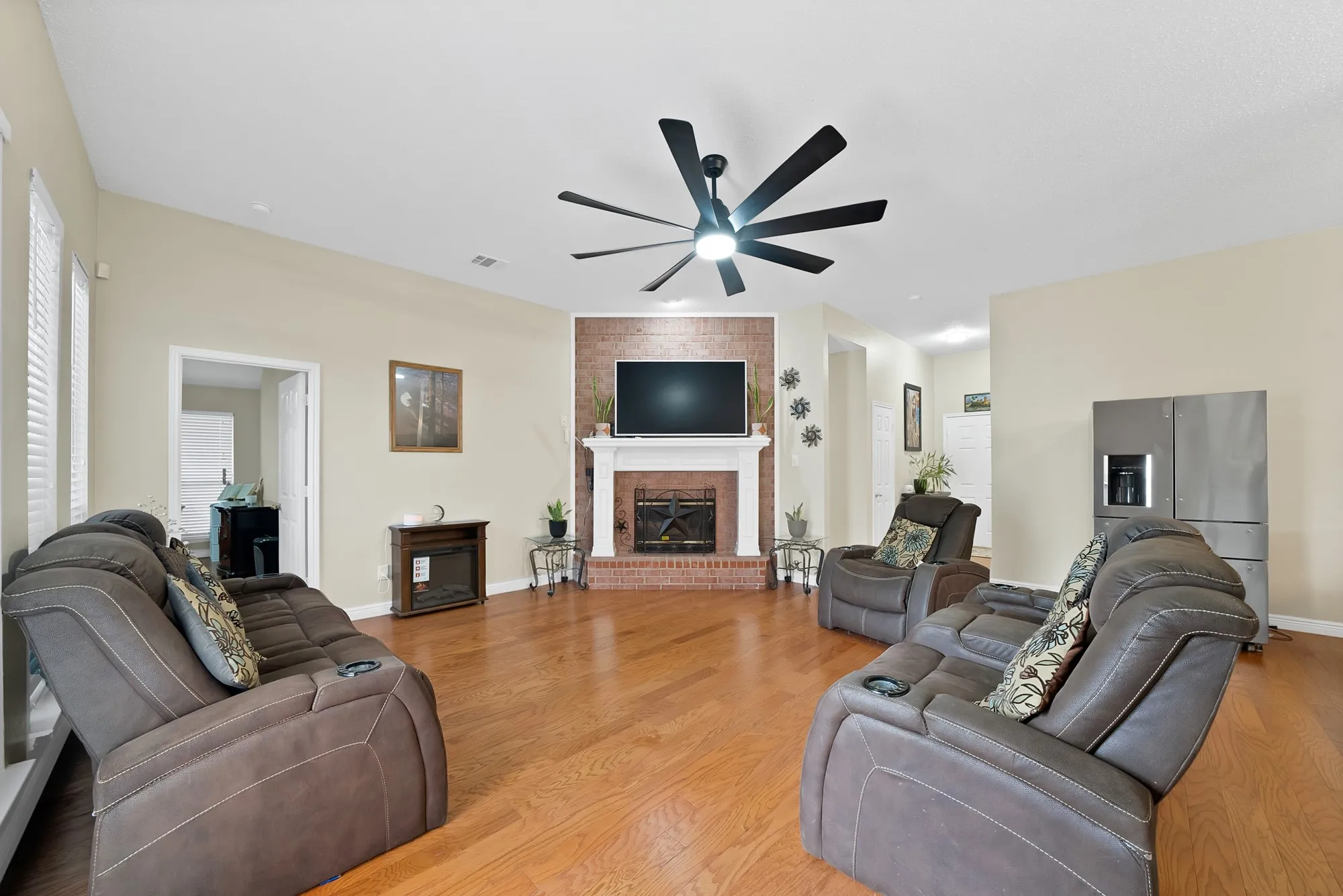 Living area featuring light wood-type flooring, a ceiling fan, and a brick fireplace