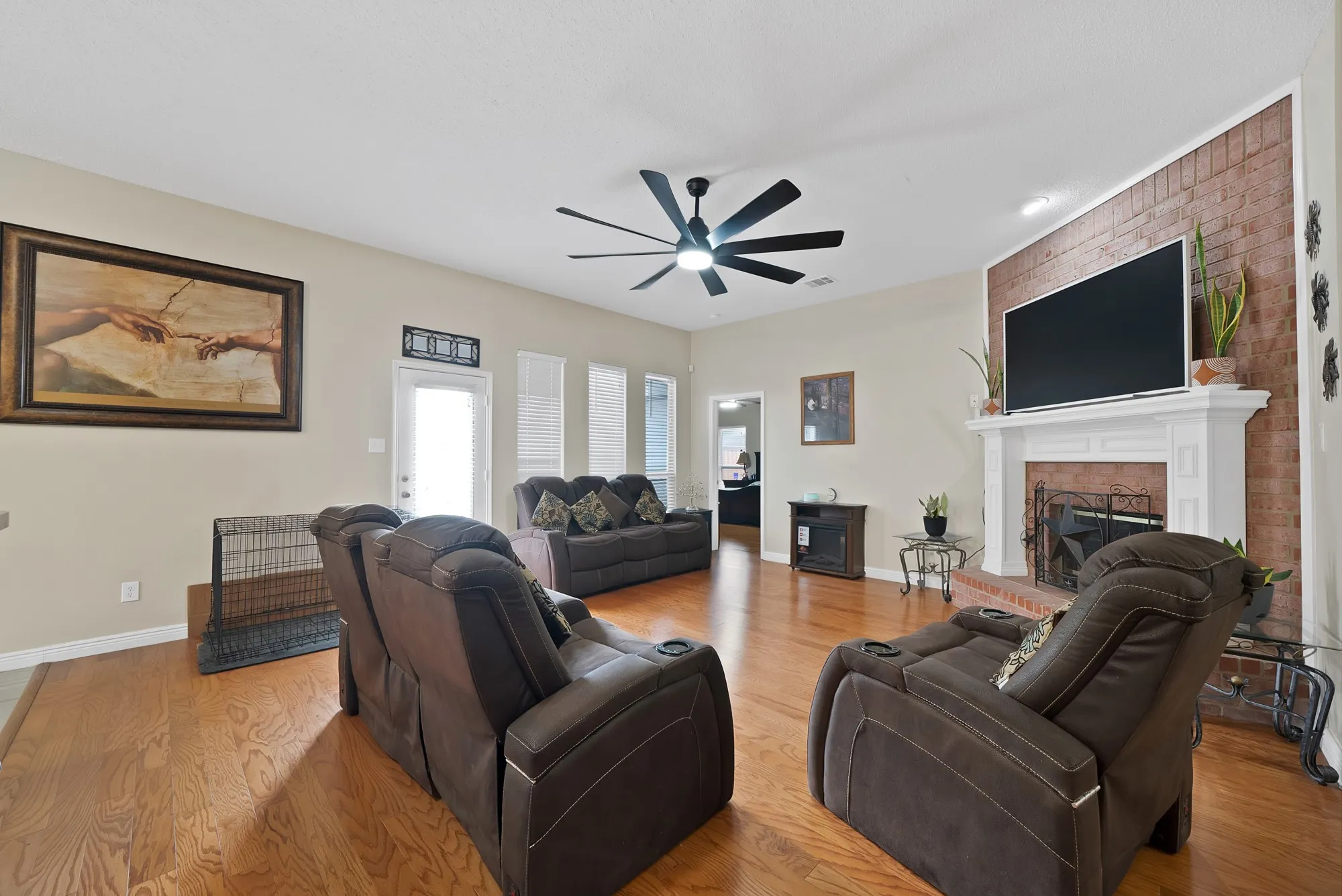 Living room featuring light wood finished floors, a brick fireplace, and ceiling fan
