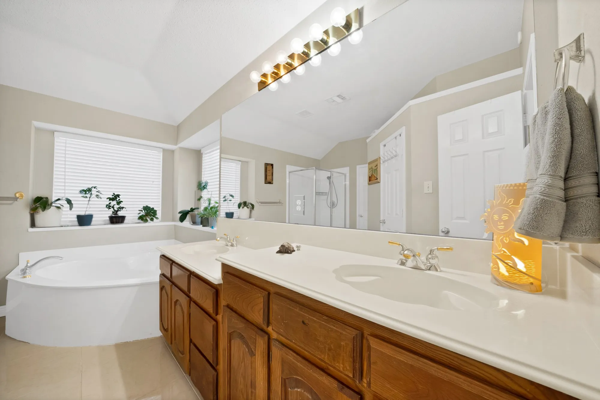 Bathroom with a garden tub, double vanity, a stall shower, light tile patterned floors, and vaulted ceiling