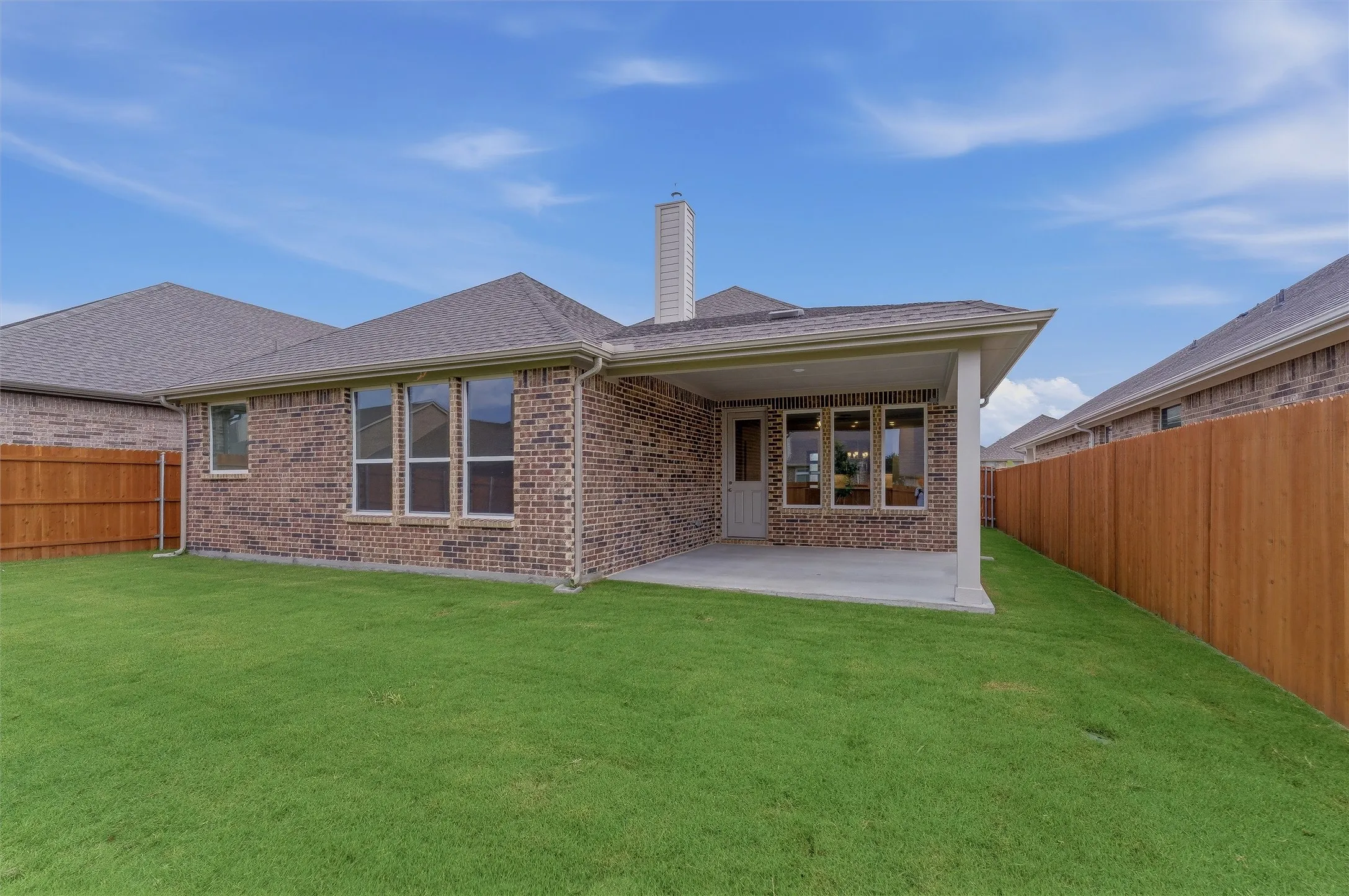 Expansive green lawn with a covered patio, brick exterior, and a privacy fence